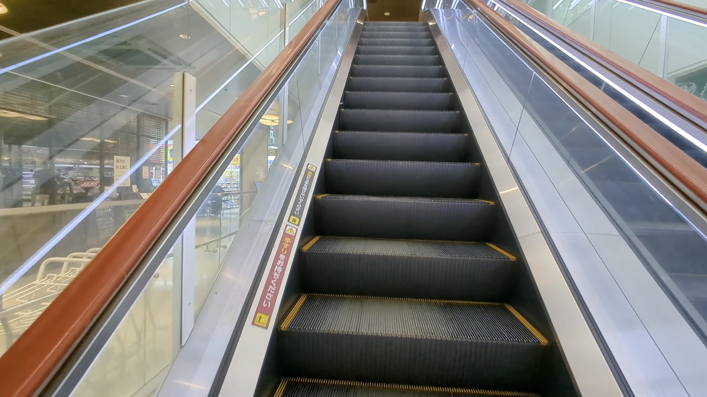 あんと西の上りエスカレーター、ガラス越しに下階のおみやげ売り場