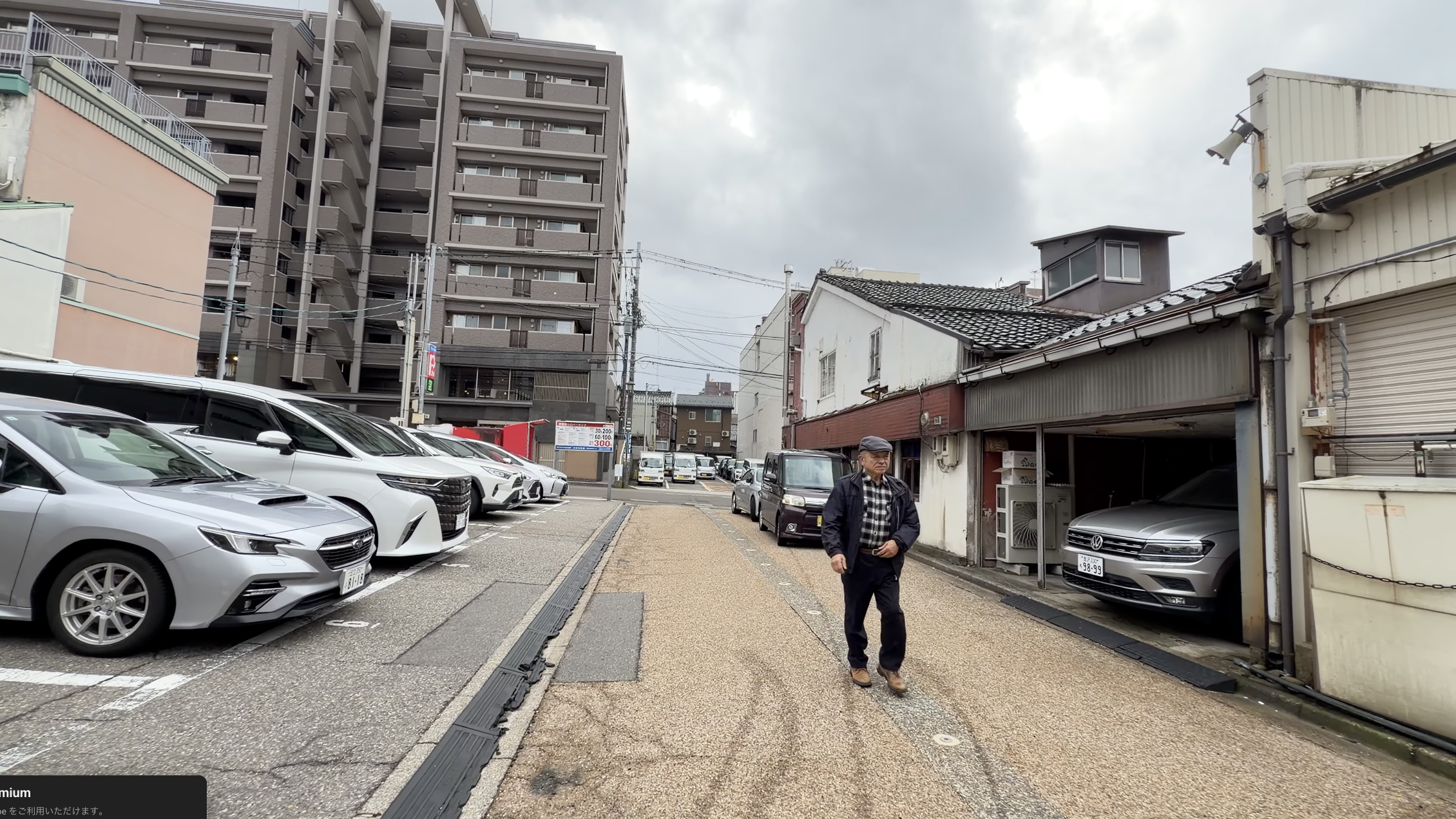 近江町市場そばの大通り、路上駐車場と歩いてくる年配の男性、奥に高層マンション