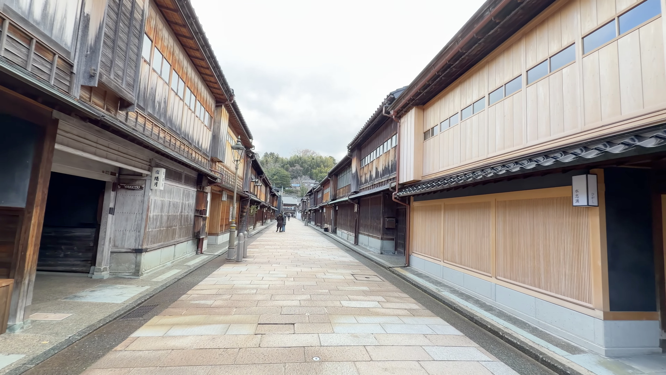 ひがし茶屋街メイン通り、両側に格子戸の木造家屋が並ぶ石畳の通り、奥に小さく歩く人影