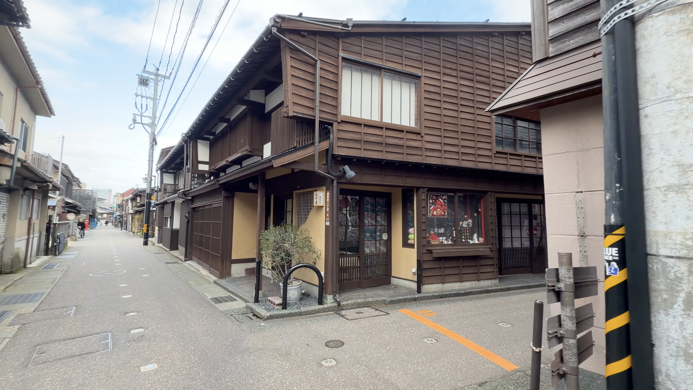 奥にメイン通りが見える路地、雑貨店の店先に飾られた小物とのれん