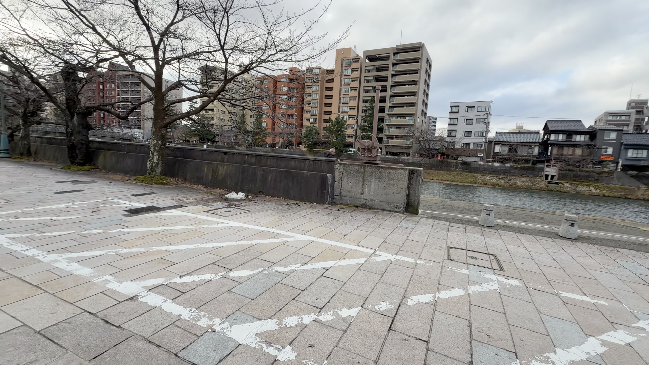浅野川沿いの遊歩道、対岸に立ち並ぶマンション群と橋、川沿いを歩く人
