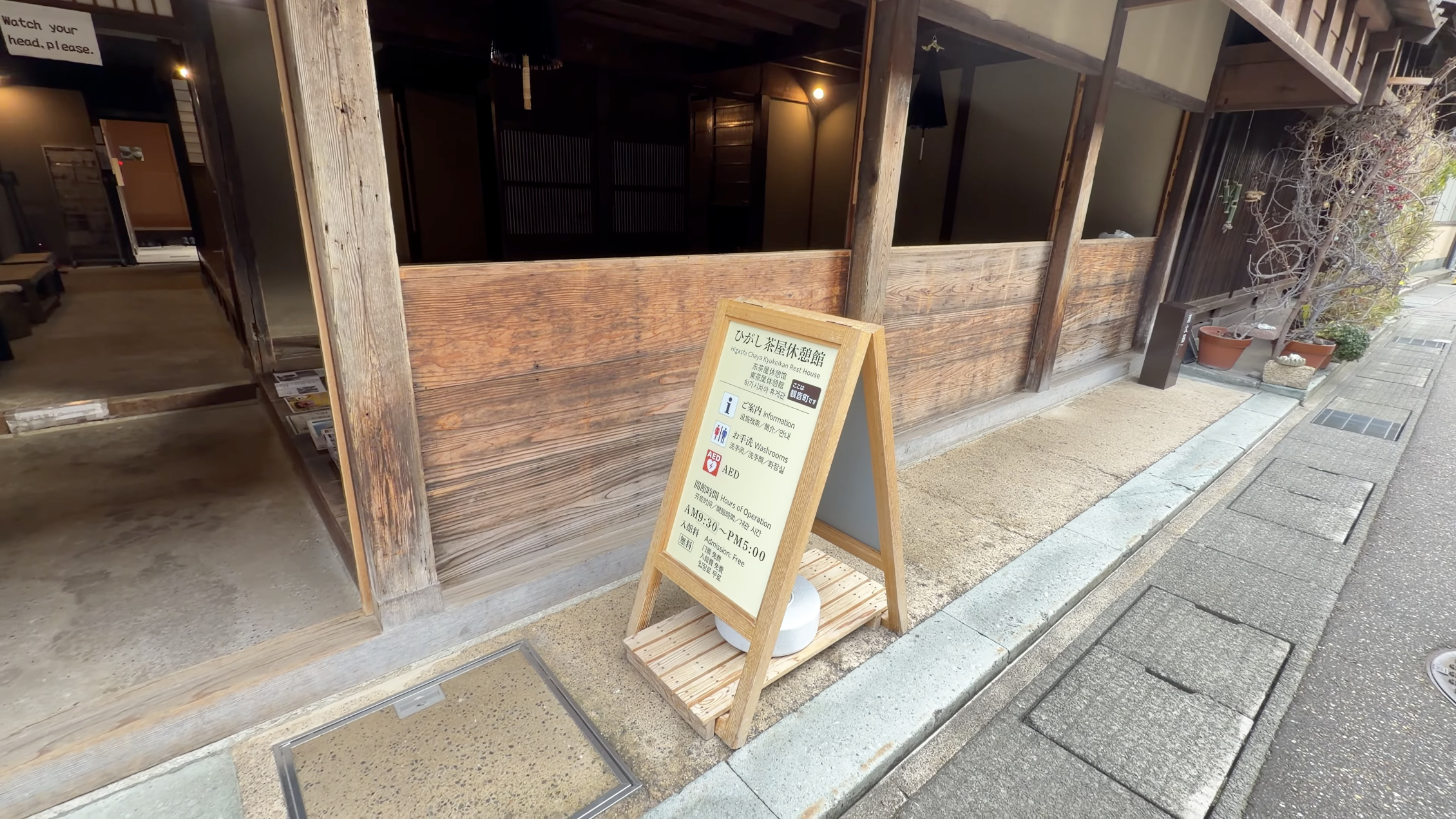 『ひがし茶屋休憩館 Higashi Chaya Kyukeikan Rest House』の案内板、木造家屋の軒下