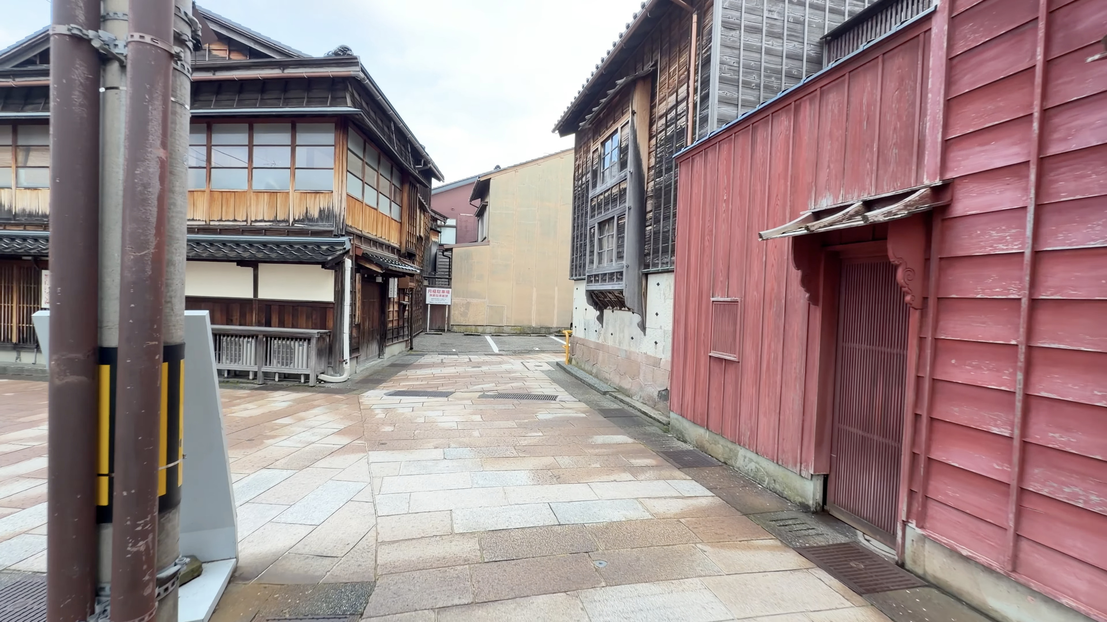 ひがし茶屋街の石畳が緩やかにカーブする路地、赤い木塀の建物と月極駐車場の看板