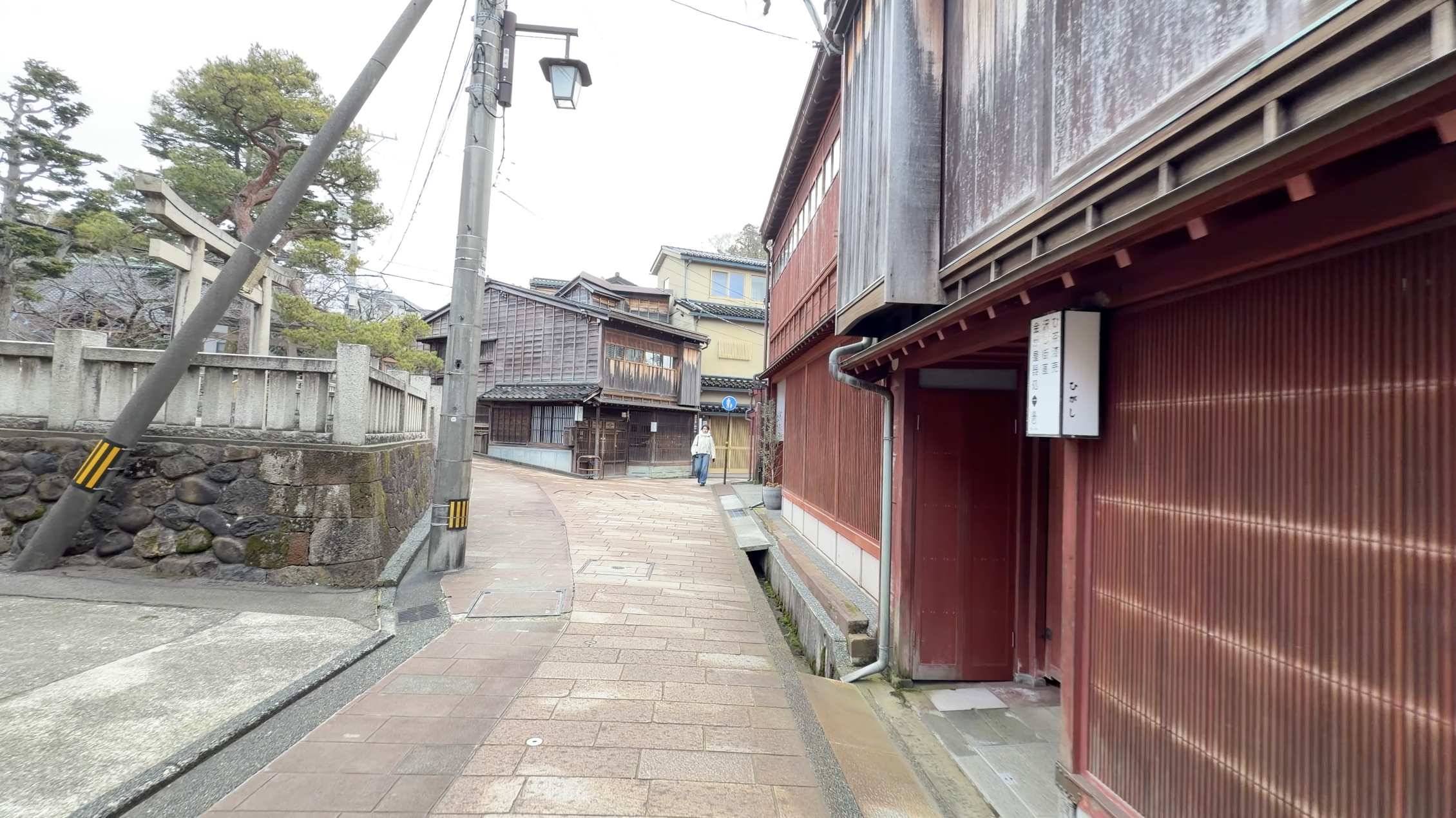 石畳の路地の左手に見える石造りの鳥居、松の木と赤い茶屋建築