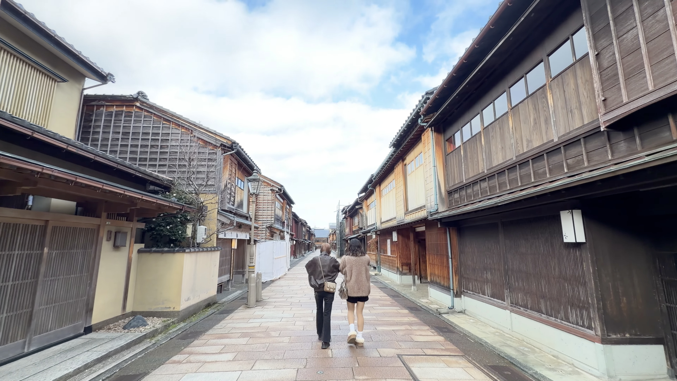 メイン通りを奥へ歩いていく二人の後ろ姿、青空とひがし茶屋街の町家が並ぶ通り