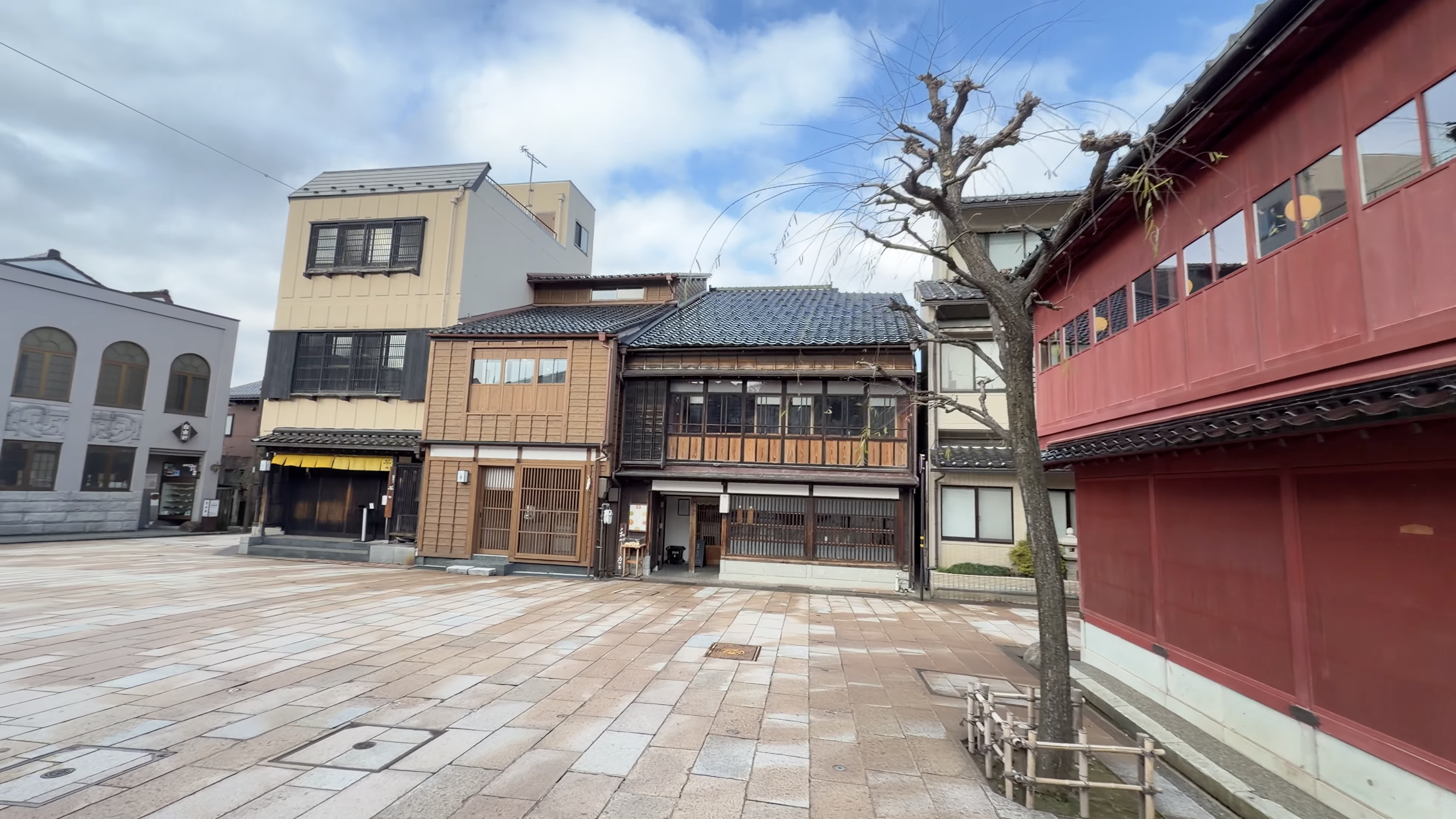 ひがし茶屋街入口の広場、青空の下に並ぶ赤い茶屋建築と町家、裸木