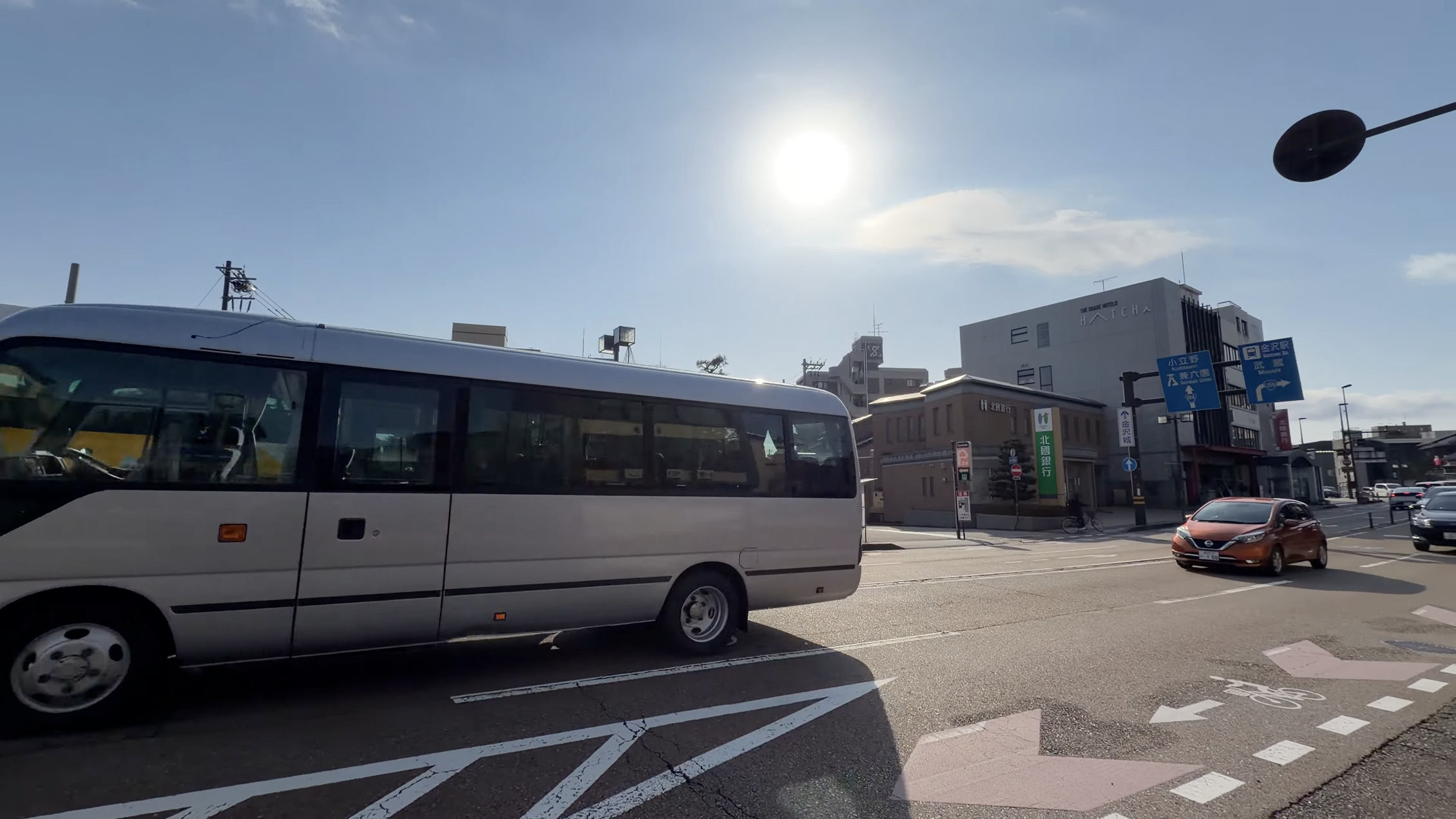 橋場町バス停付近の交差点、路線バスと北國銀行の建物、金沢駅方面を示す青い案内標識