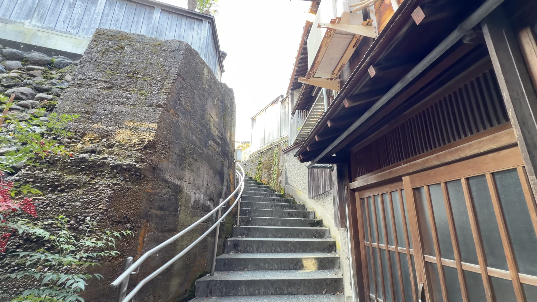 コンクリートの石垣に沿ってのぼる「あかり坂」の階段、右手に木造家屋の格子戸、明るい日差し