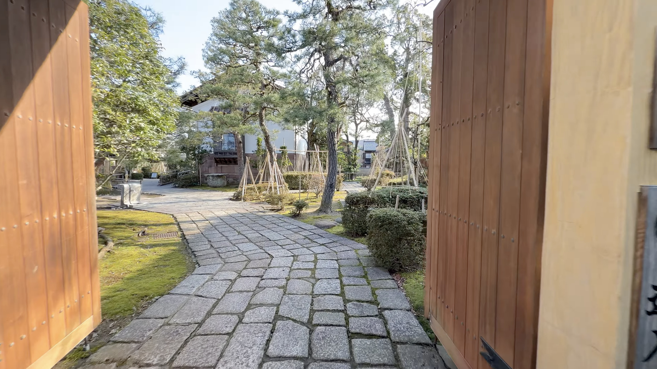 彦三緑地の入り口、雪吊りされた松の木々と苔むした庭園、奥に武家屋敷風の建物