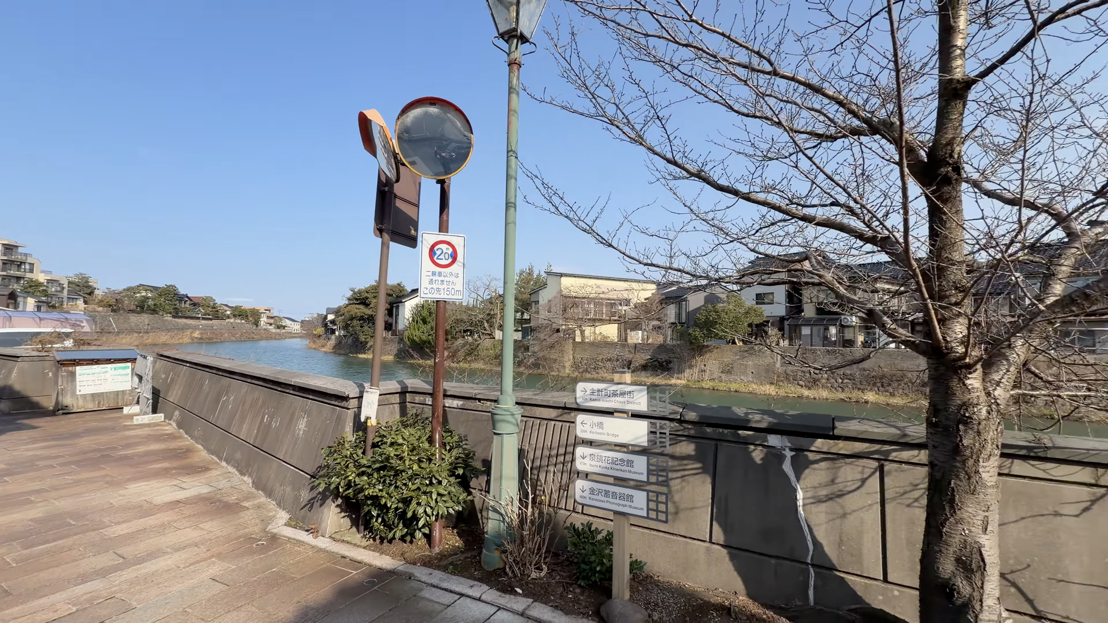 浅野川沿いの案内標識、「主計町茶屋街」「小橋」「泉鏡花記念館」「金沢蓄音器館」の方向表示、奥に川面