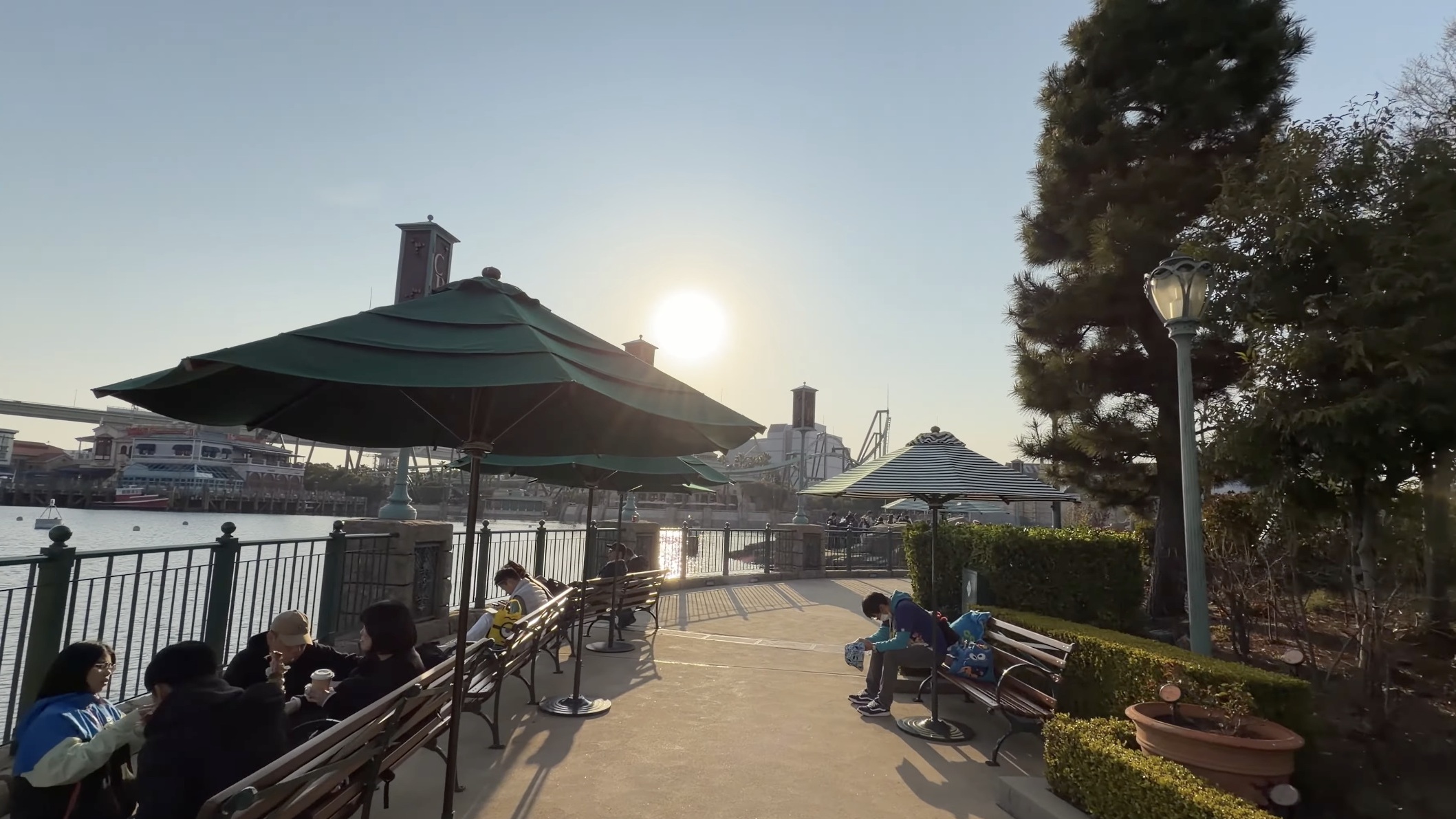 ラグーン沿いの緑のパラソルとベンチ、夕日を浴びる人たち