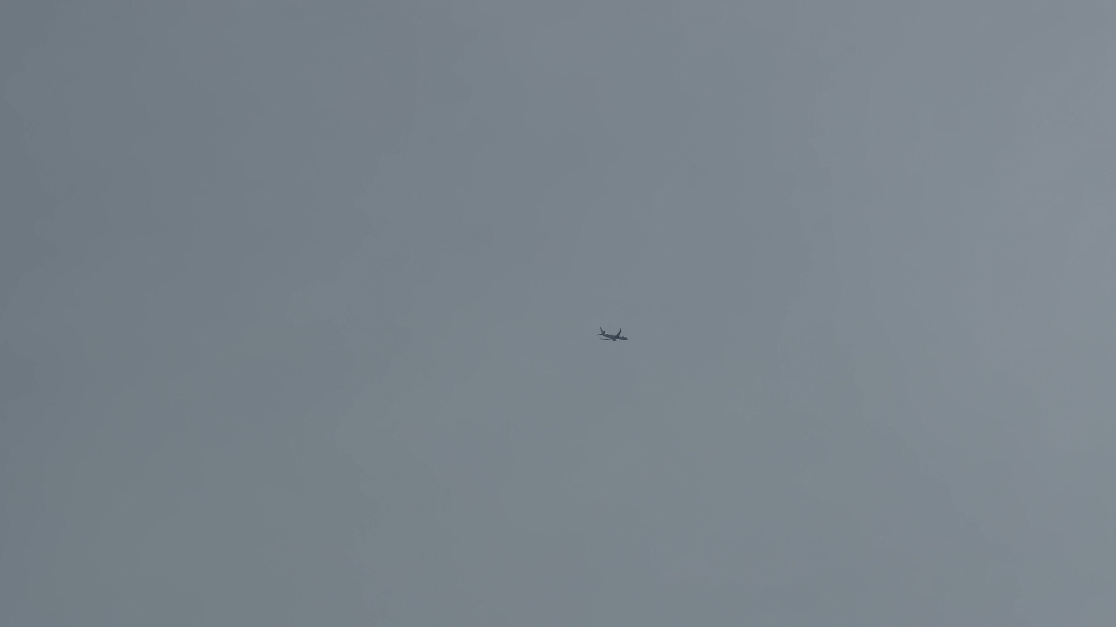 灰色の空に小さく見える飛行機のシルエット