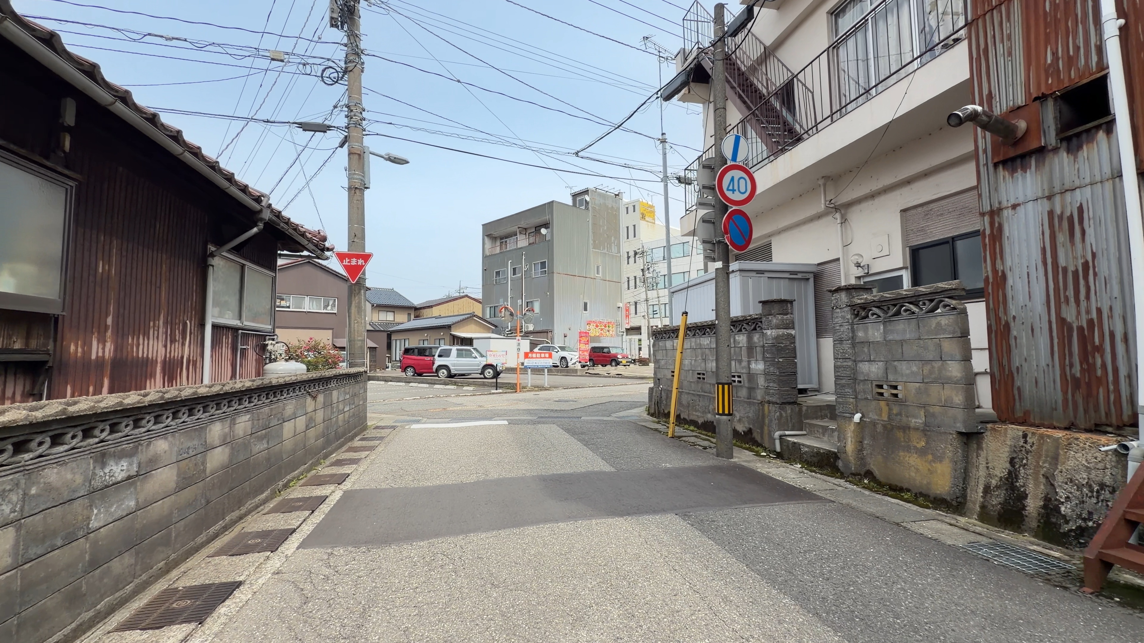 板壁とサビたトタンの古い建物が並ぶ路地、「止まれ」の標識