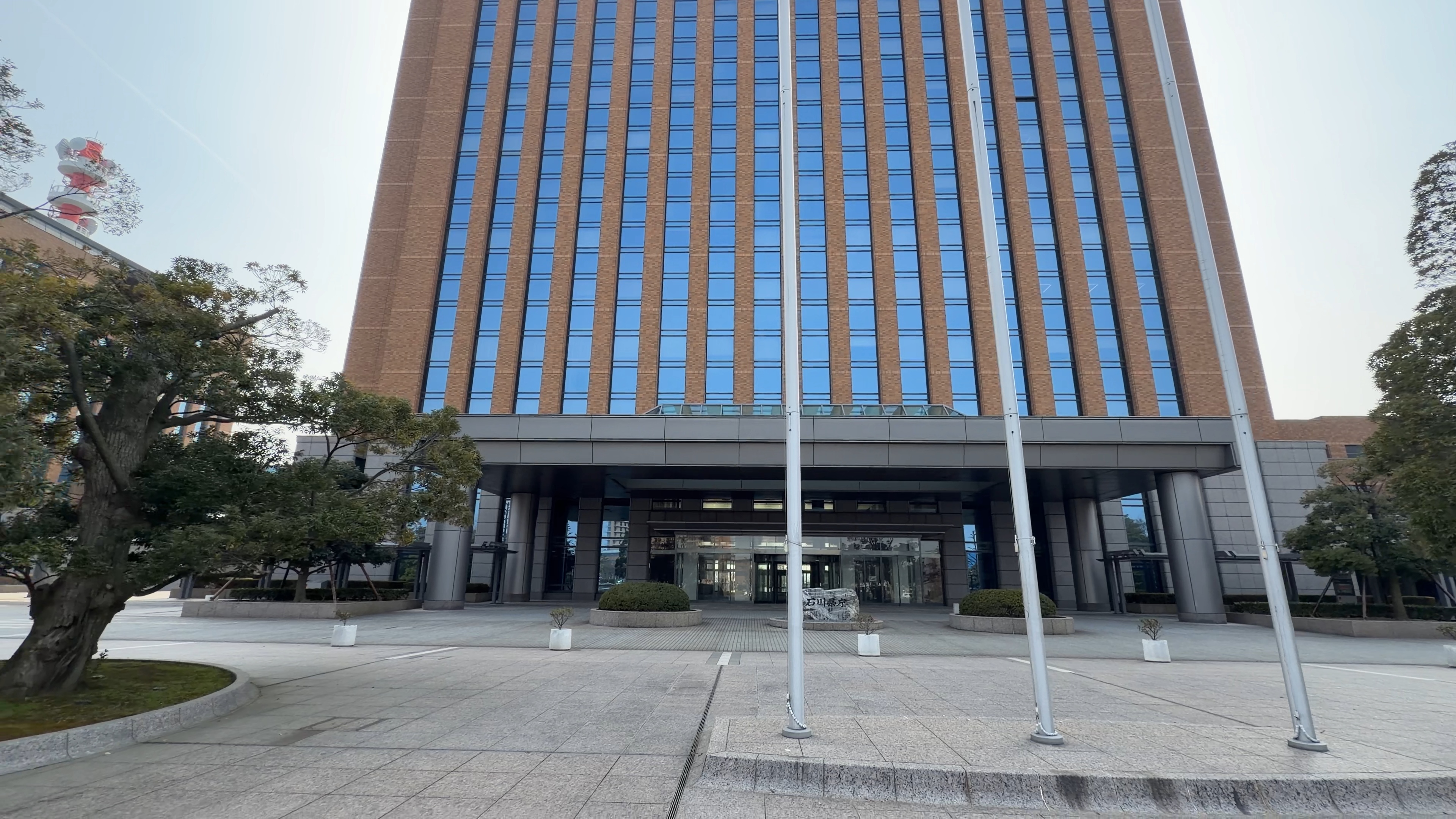 石川県庁 行政庁舎の正面、石川県庁の石碑と旗竿が並ぶ
