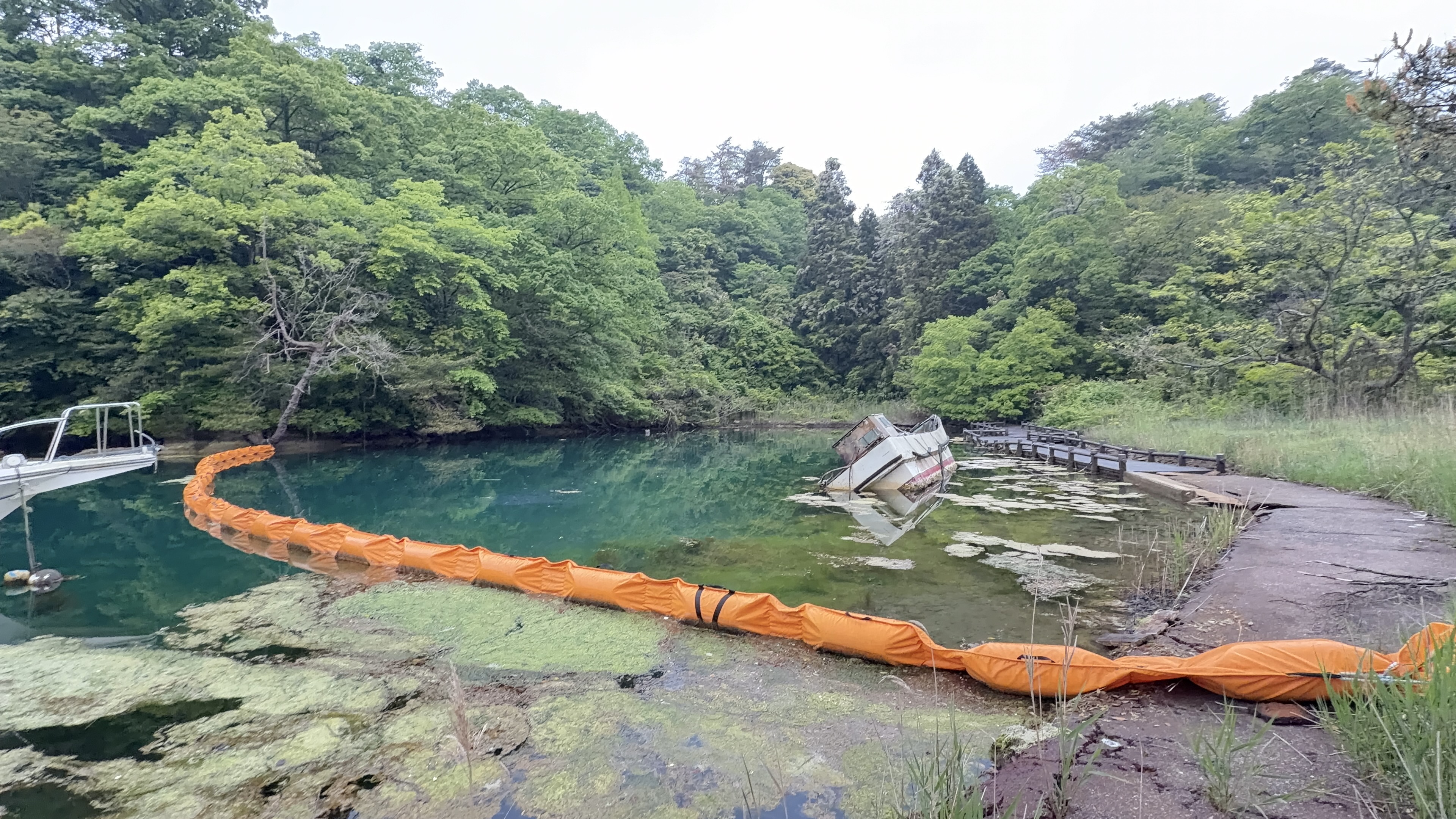 オレンジ色のオイルフェンスが水面を仕切る入り江