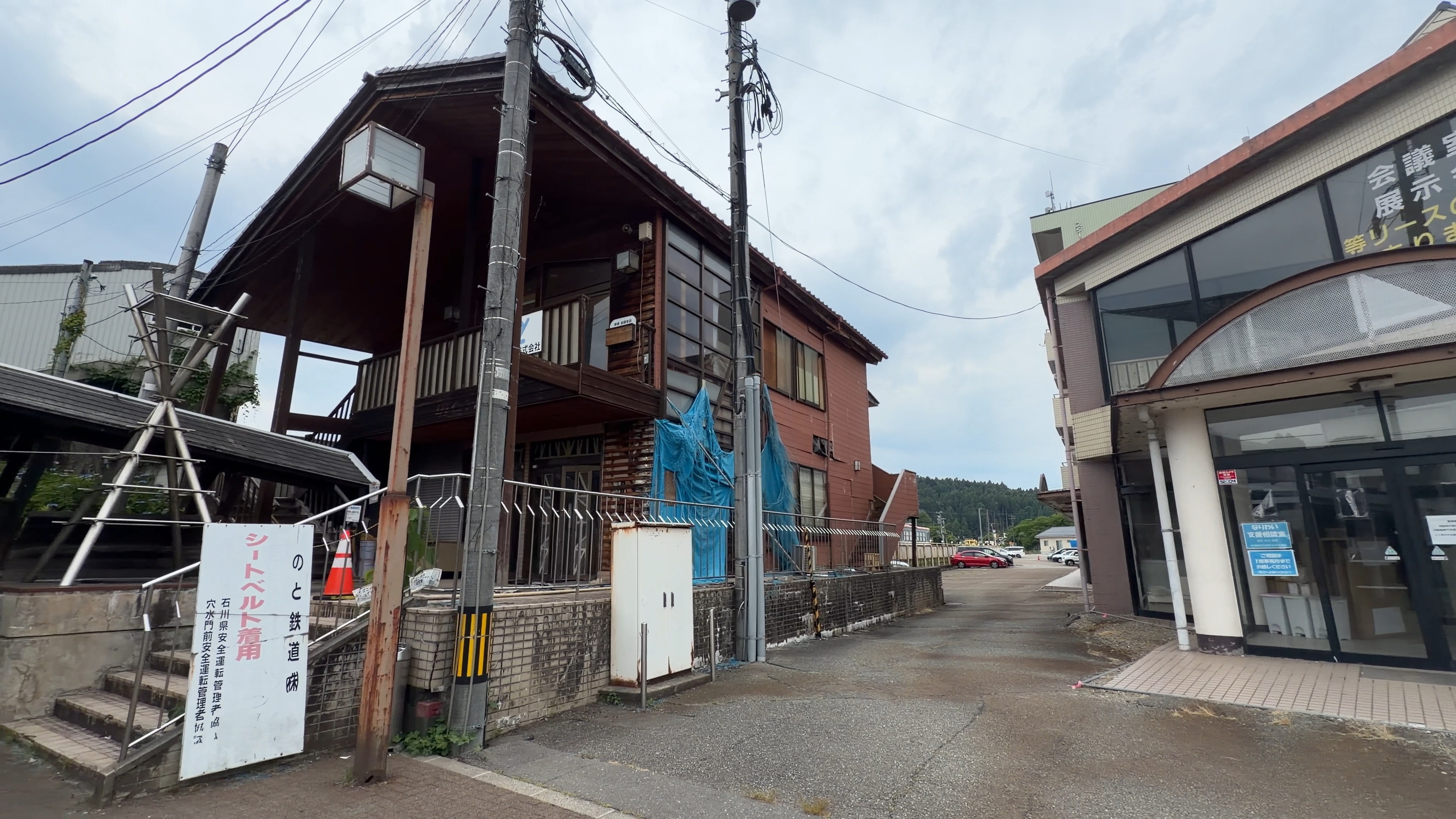 駅の横に建つ古い木造建物、青いブルーシートと足場、傾いた建物