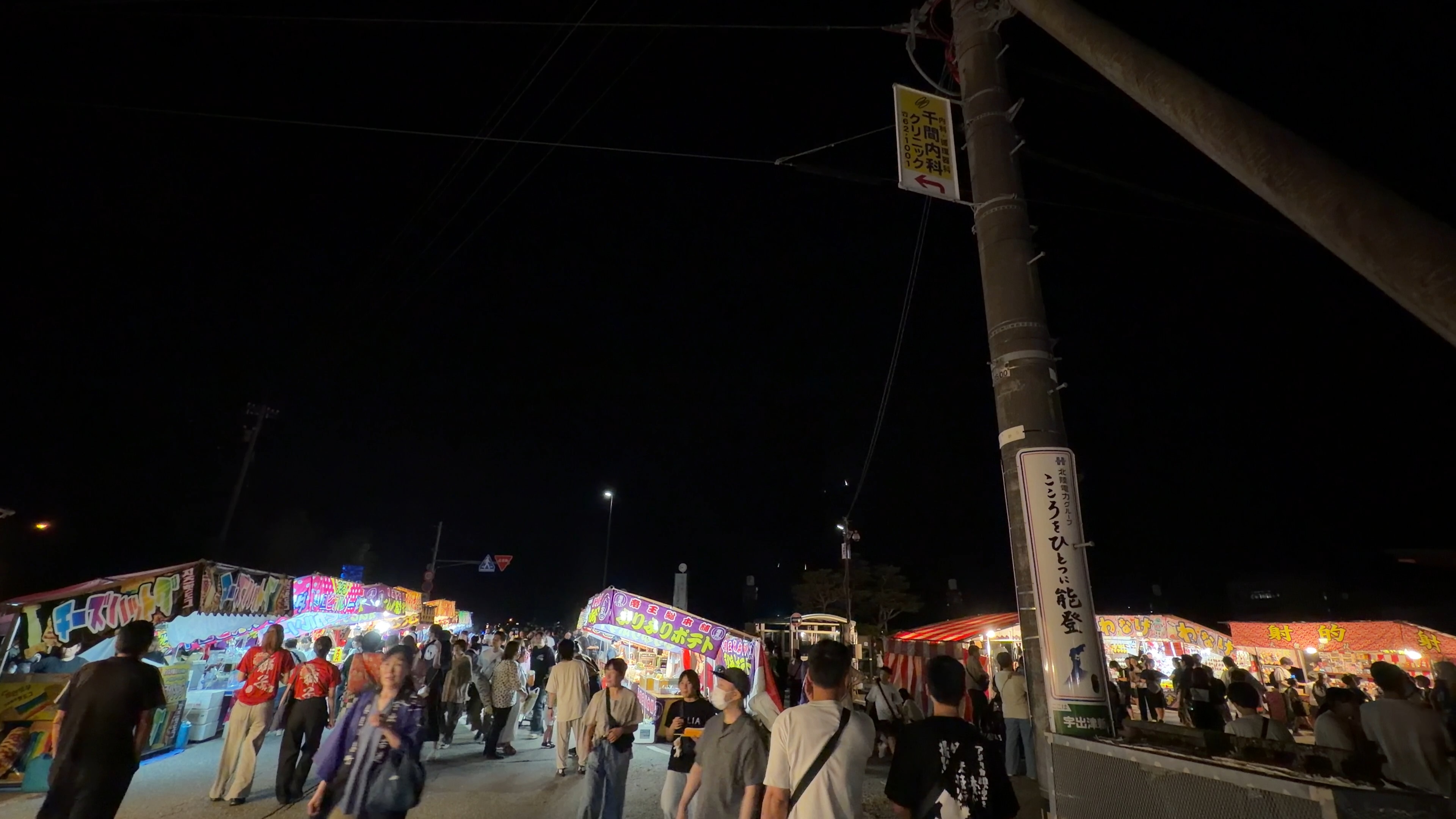 色とりどりの屋台の看板が並ぶ夜の通り、大勢の人でにぎわう