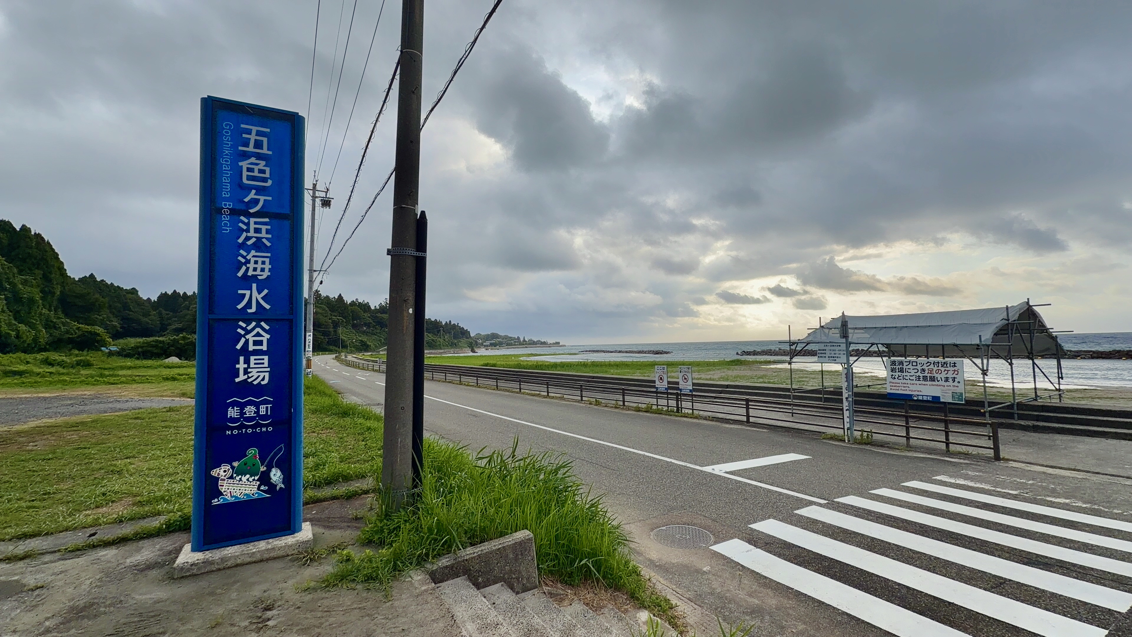 どんより曇った空の下、五色ケ浜海水浴場の看板と海沿いの道