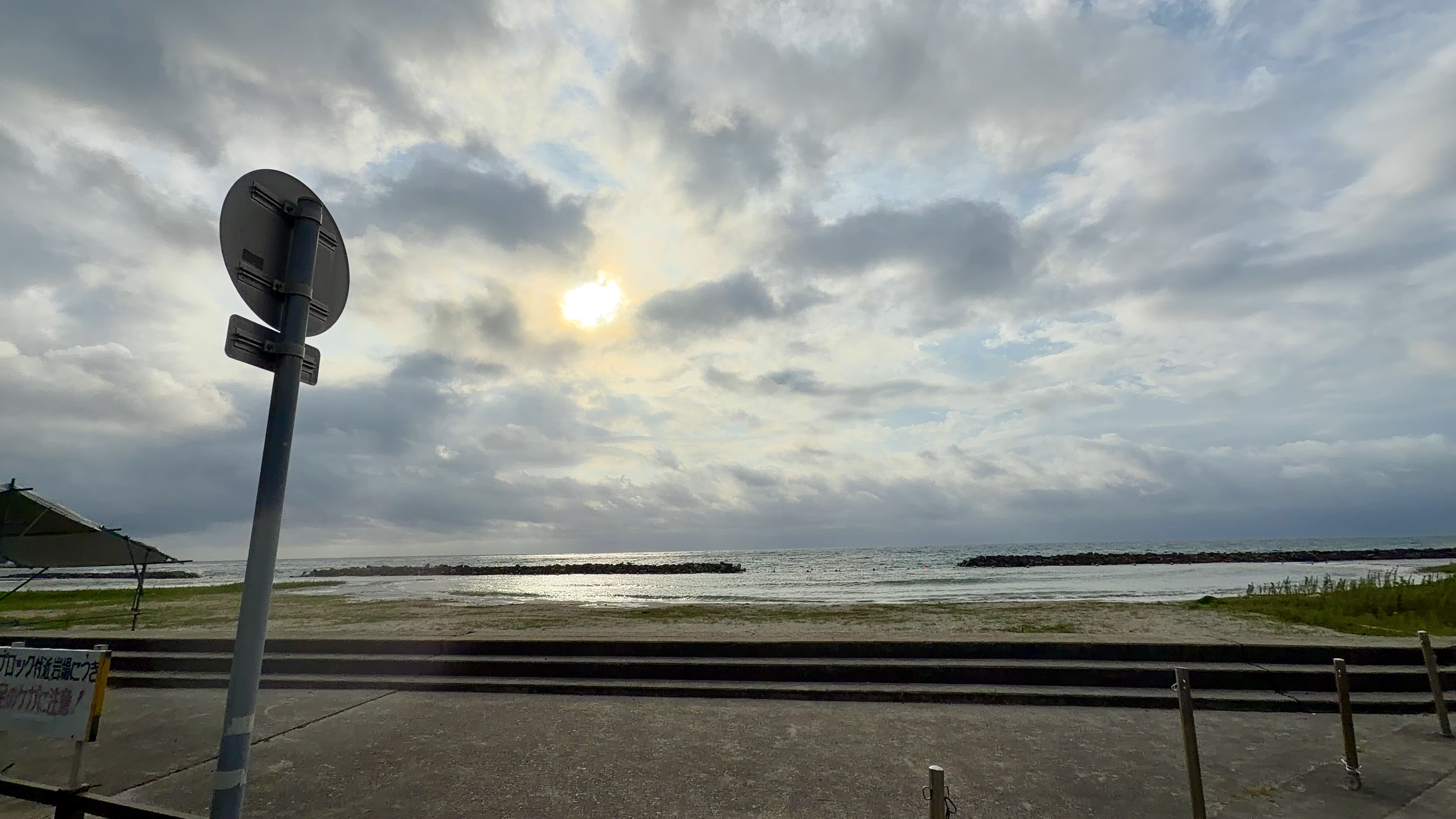 雲の切れ間から光がさす五色ケ浜、海水浴場の標識の一部が見える