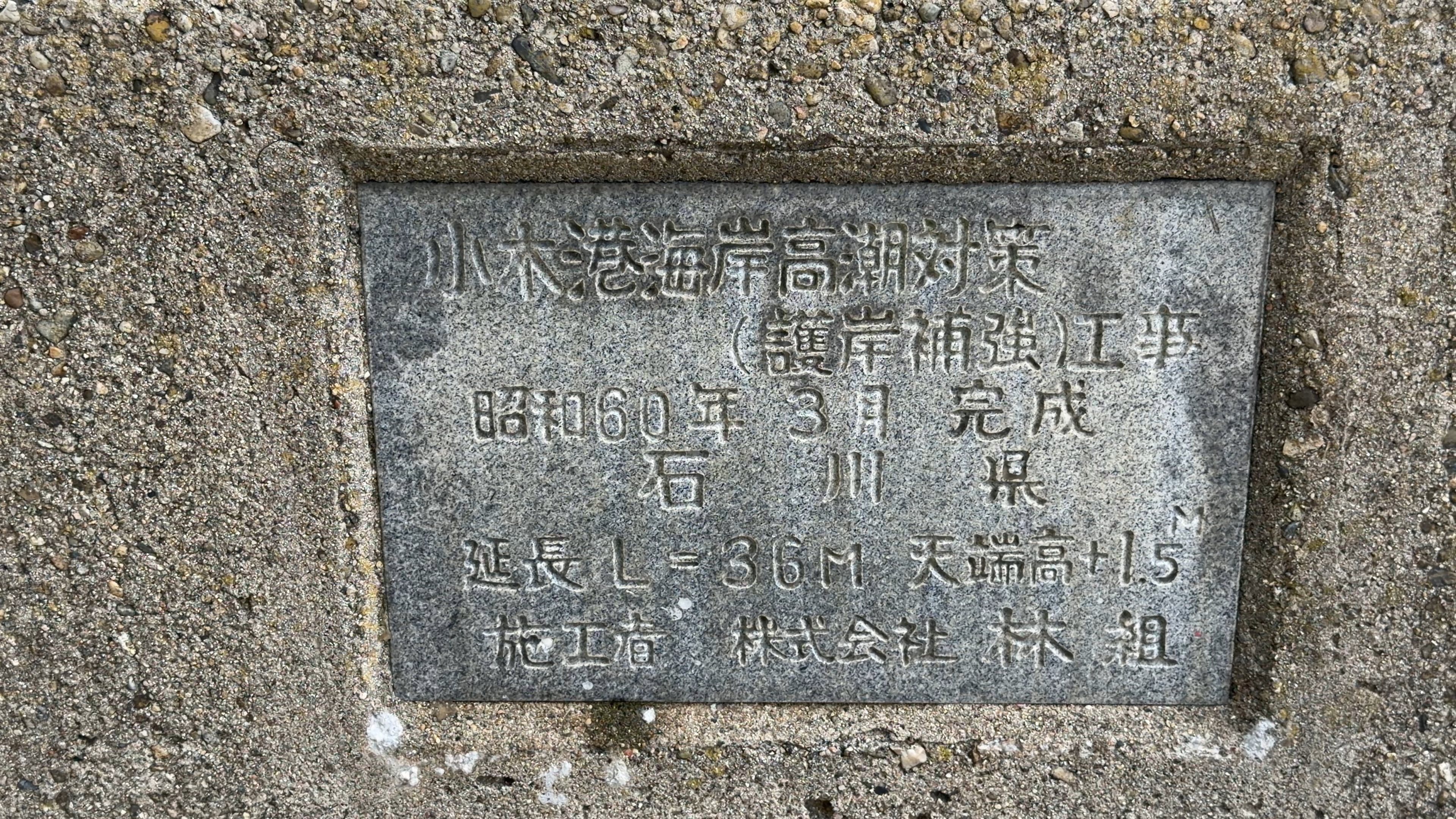 石に刻まれた「小木港海岸高潮対策（護岸補強）工事 昭和60年3月完成」の碑文