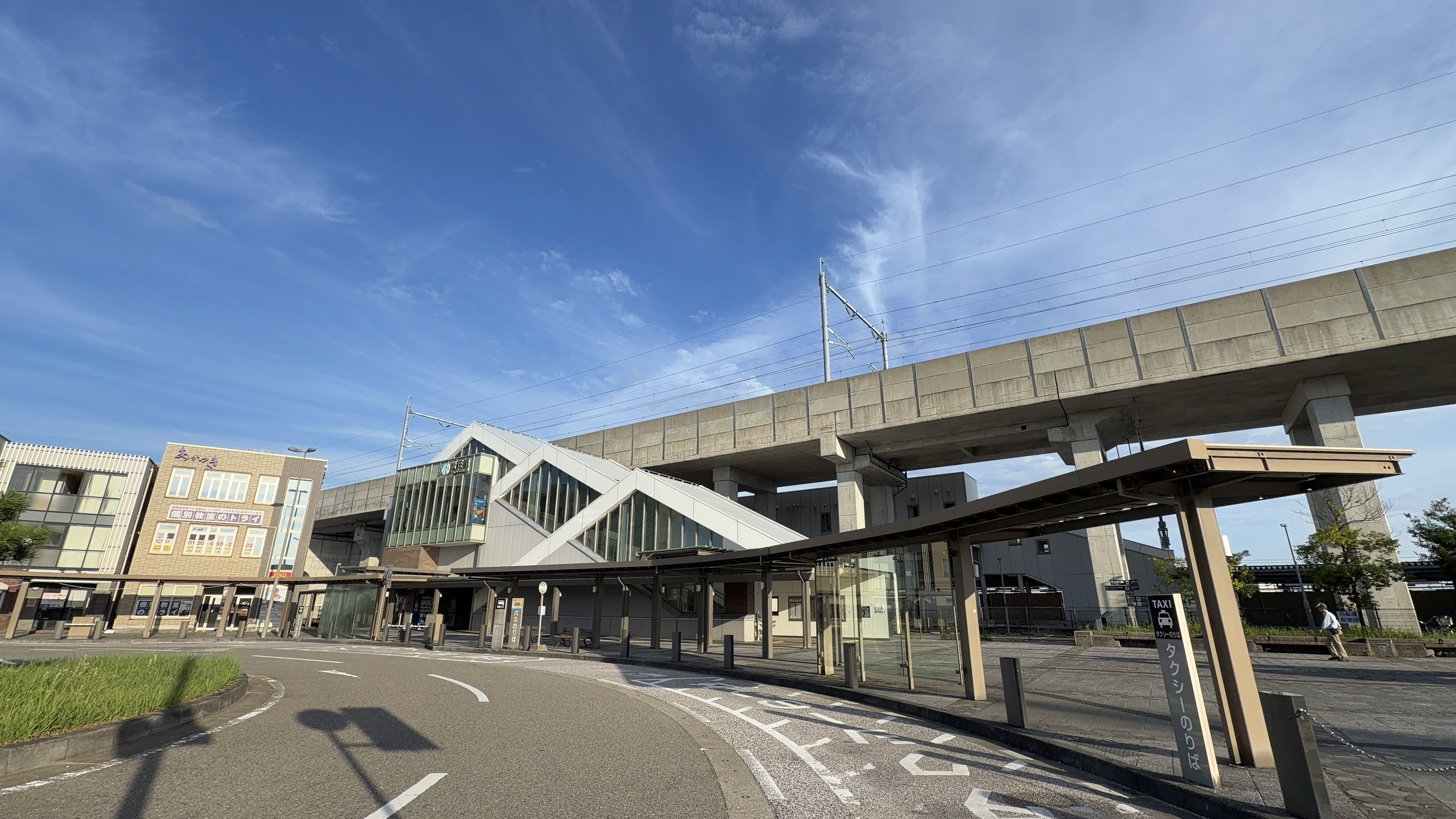 松任駅南口、白い三角の屋根の駅舎と高架、タクシー乗り場、青空