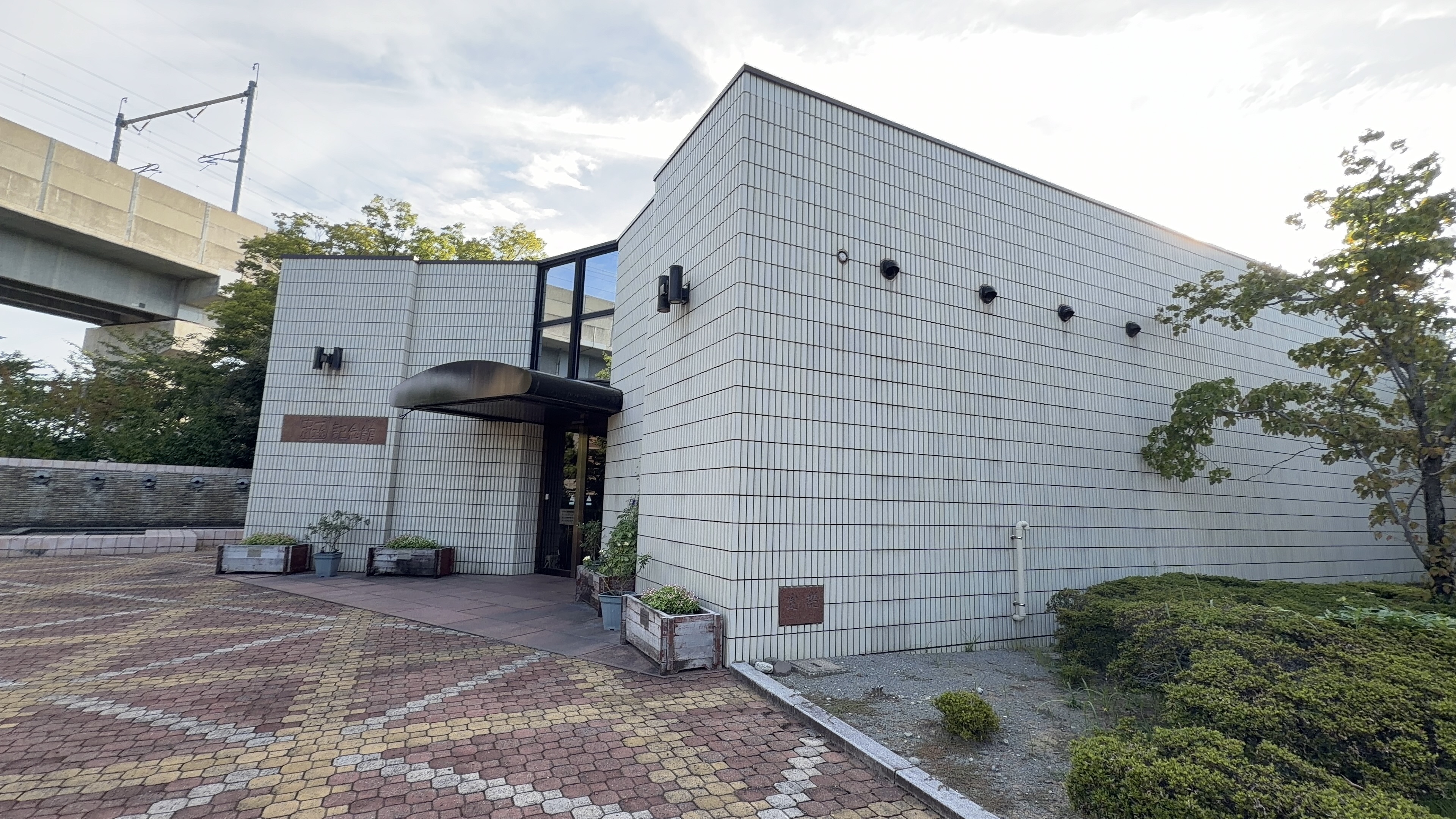 中川一政記念美術館の建物、白いタイル張りの外壁、高架の下、玄関に木の庇
