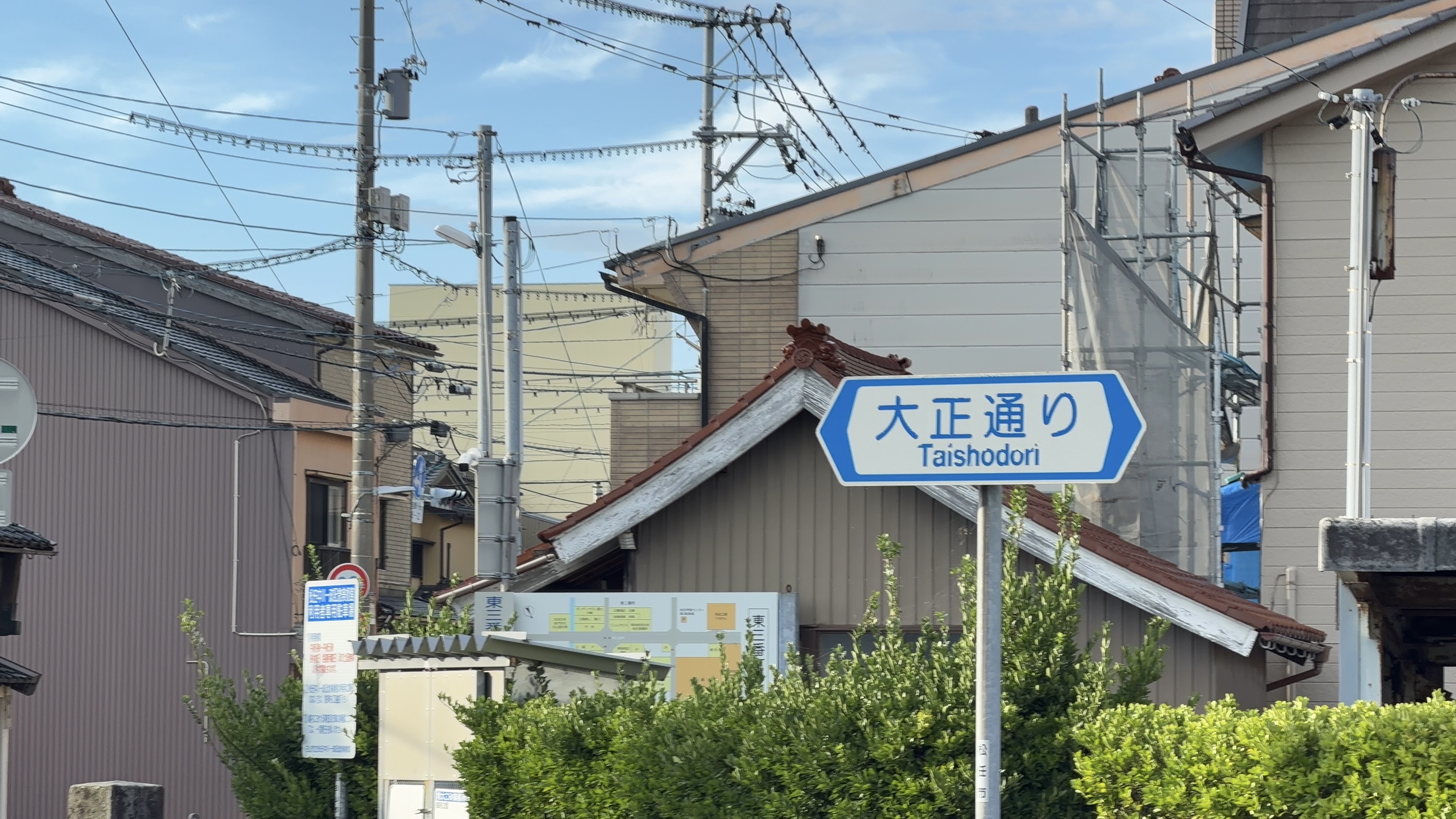「大正通り Taishodori」の標識、瓦屋根の民家越しに朝日