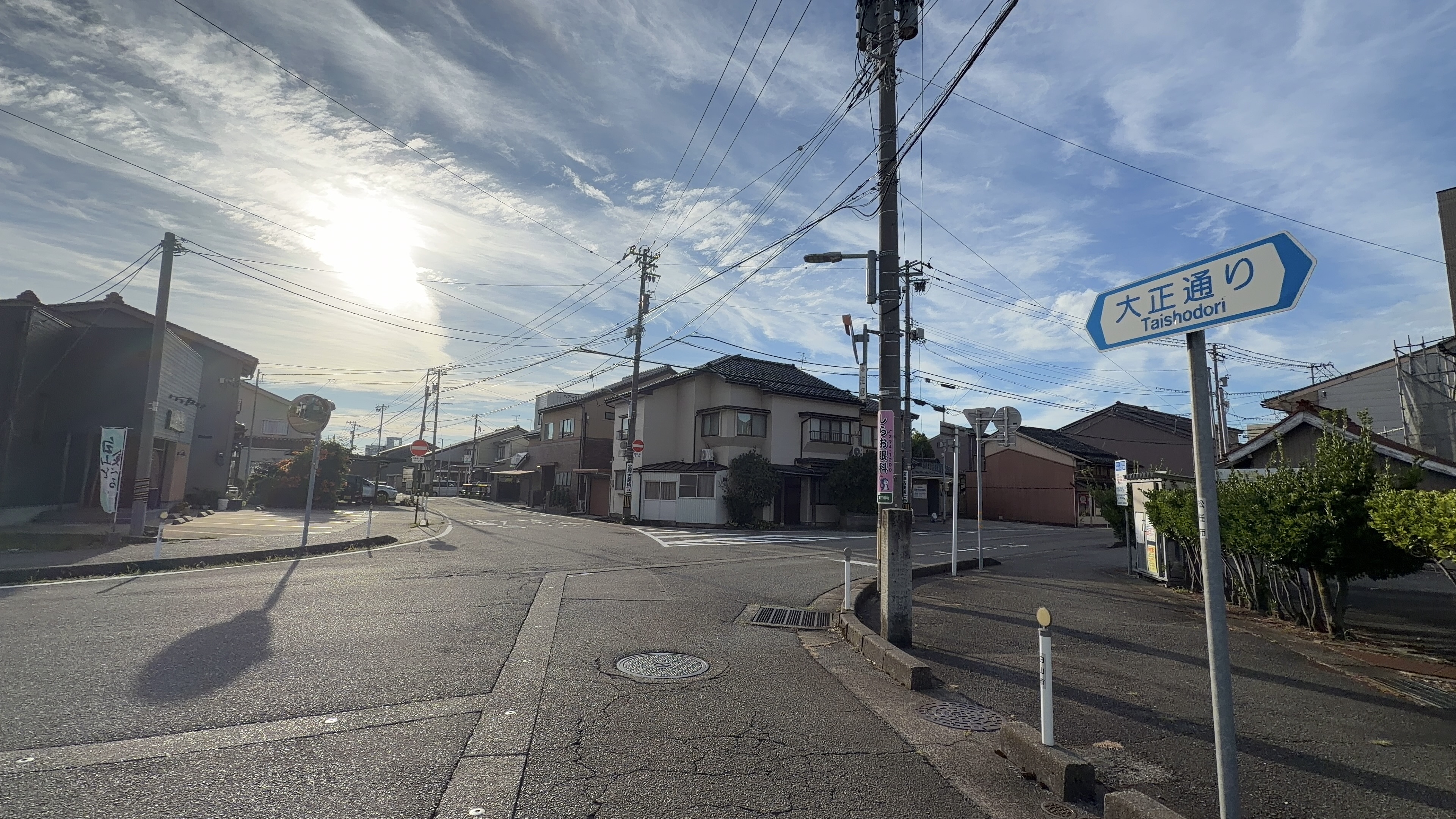 大正通りの交差点、逆光の朝日、両脇に民家が並ぶ静かな住宅街