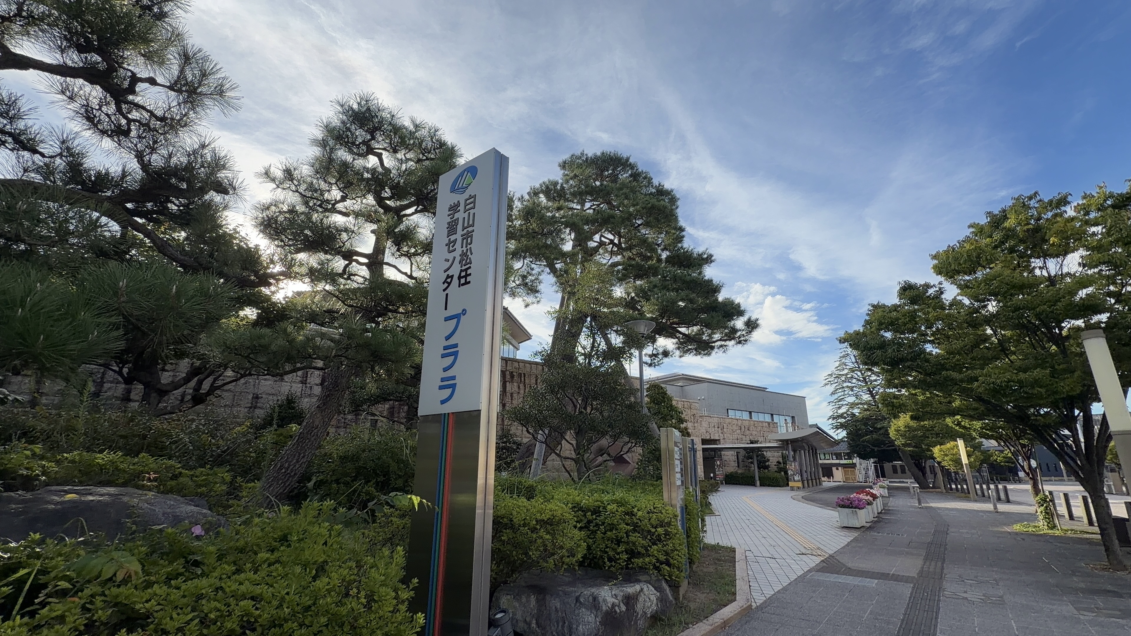 「白山市松任学習センター プララ」のサイン、大きな松の木、奥に石張りの建物