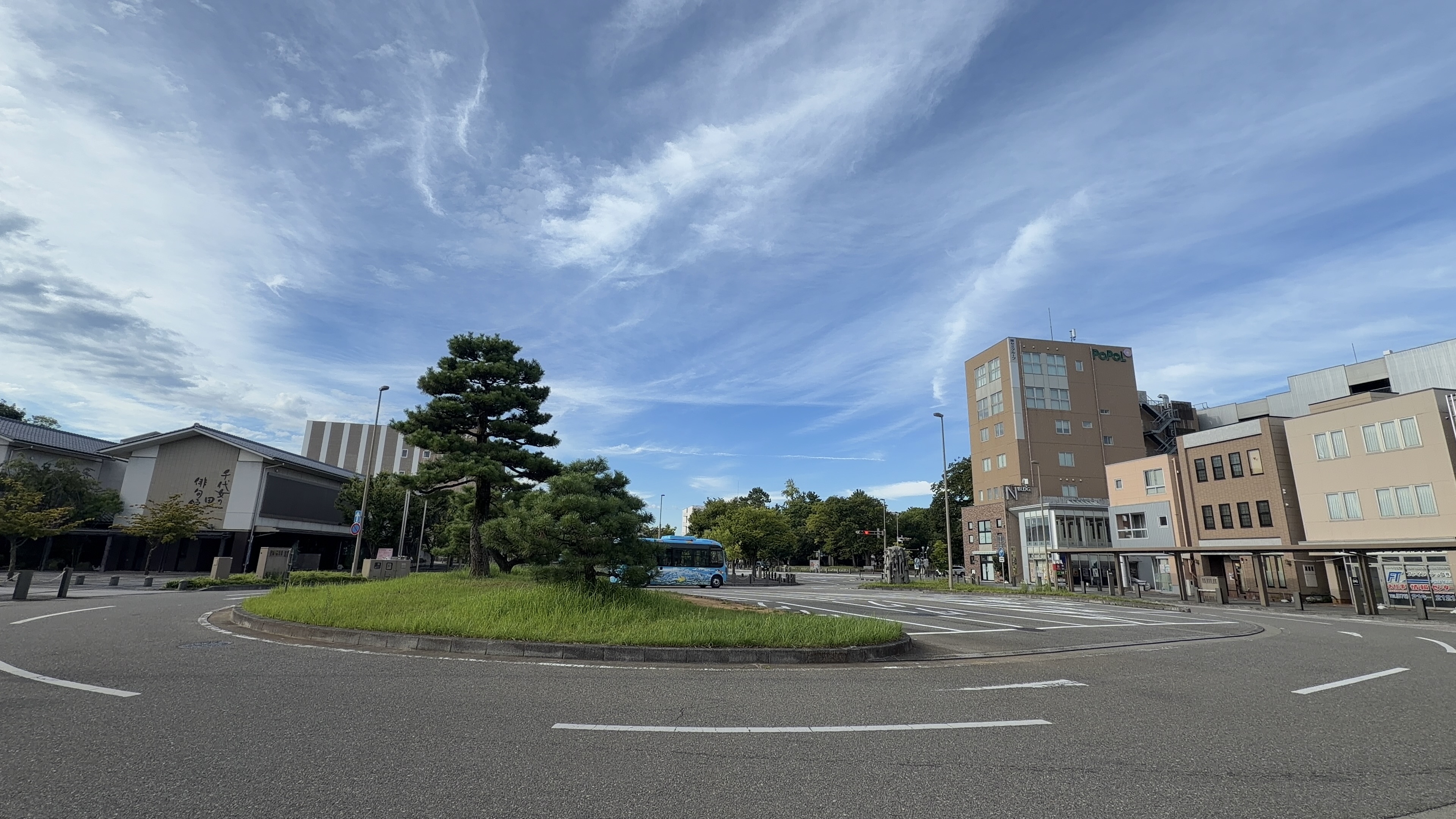 松任駅前のロータリー、松と青いコミュニティバス、奥にPoPoLビル