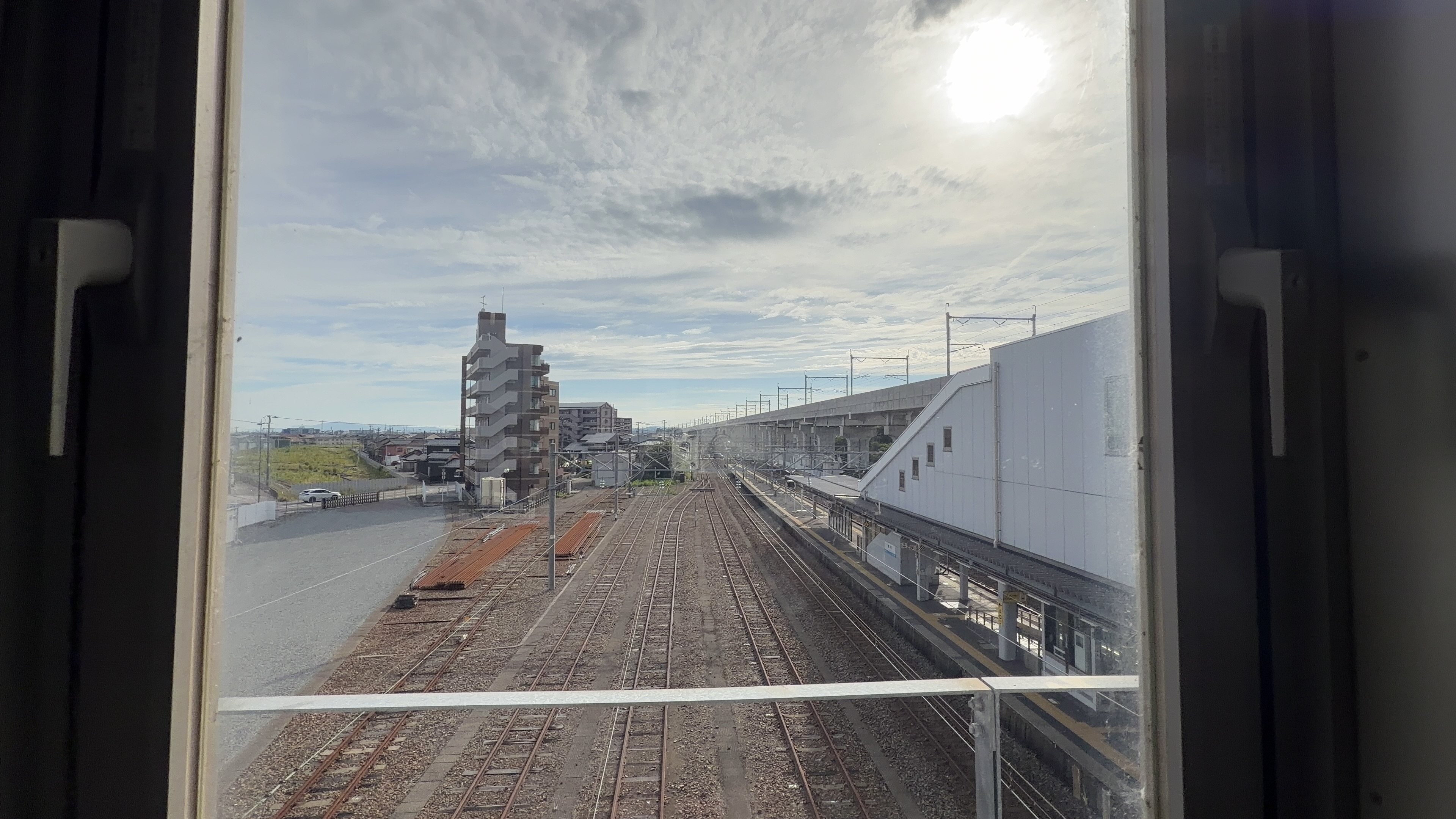 別の窓から見下ろす線路とホーム、白い屋根の建物と太陽