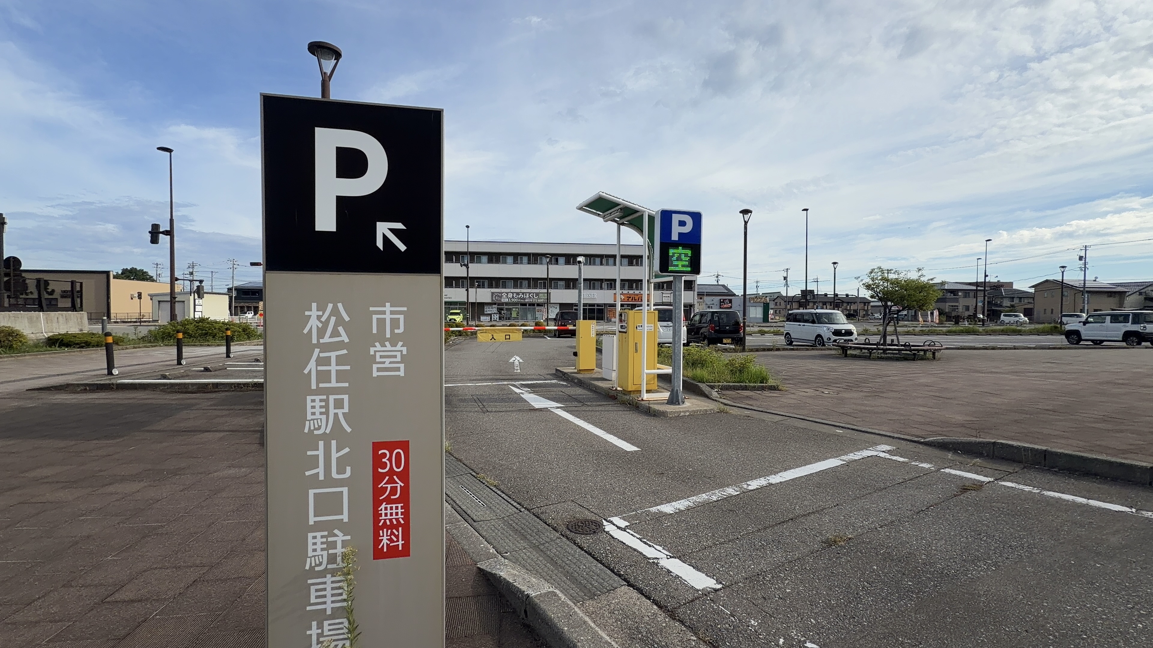 「市営 松任駅北口駐車場 30分無料」の案内標識、奥に駐車場とゲート