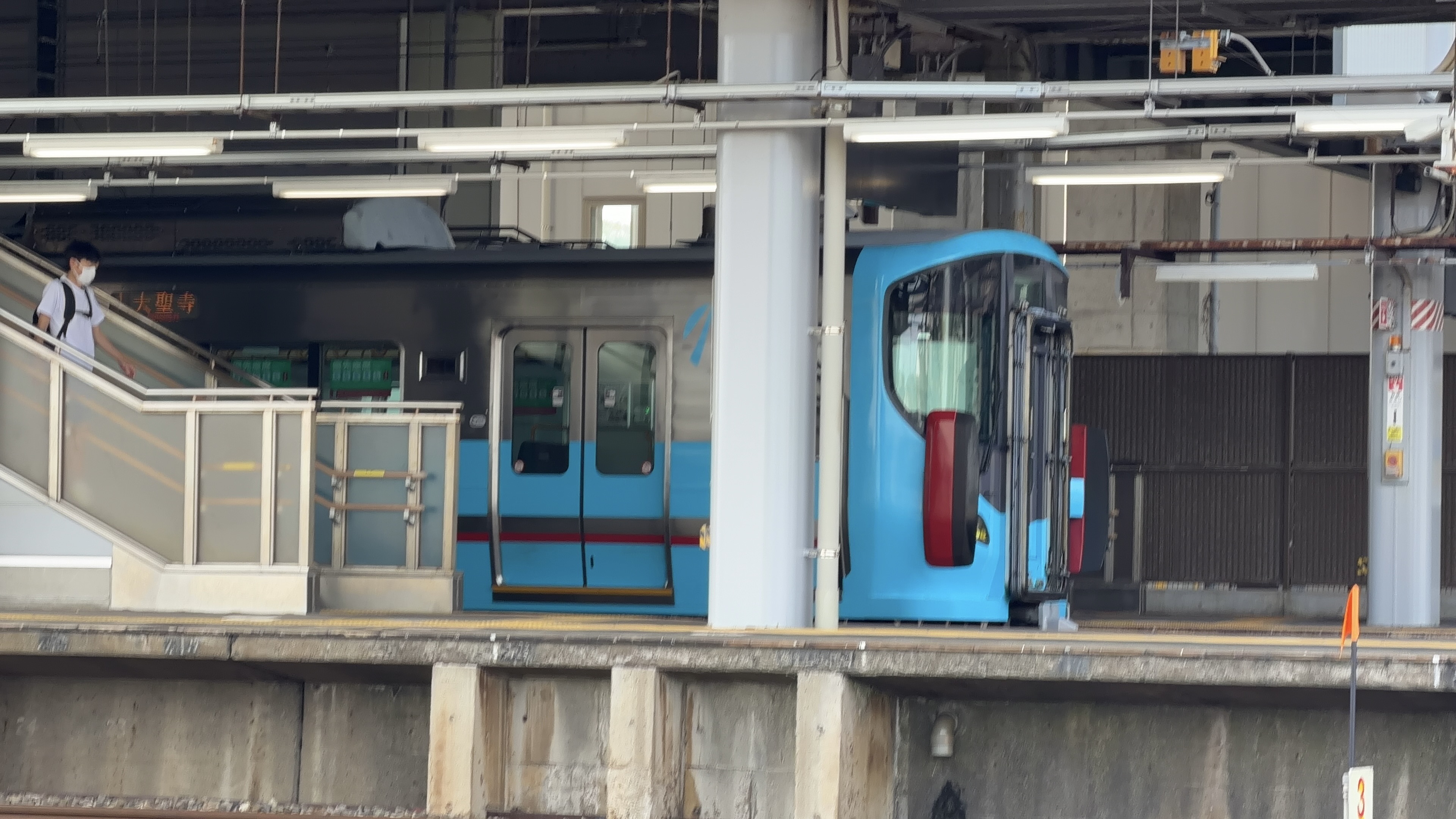ホームに停車する青い車両、行き先表示「大聖寺」とエスカレーターを降りる乗客