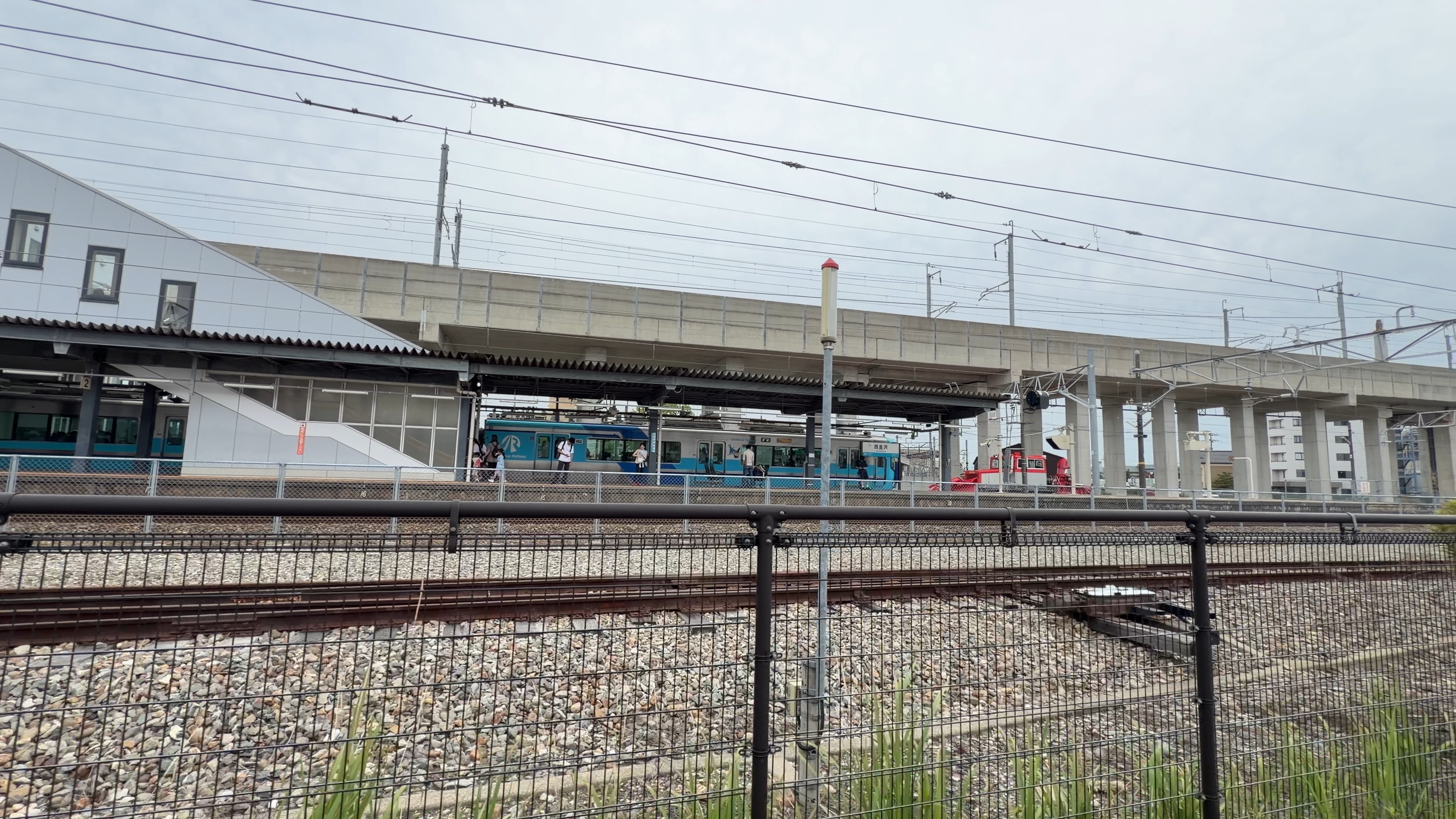 IRいしかわ鉄道の青い車両と、ホームから降りる高校生たち、奥に赤い車両
