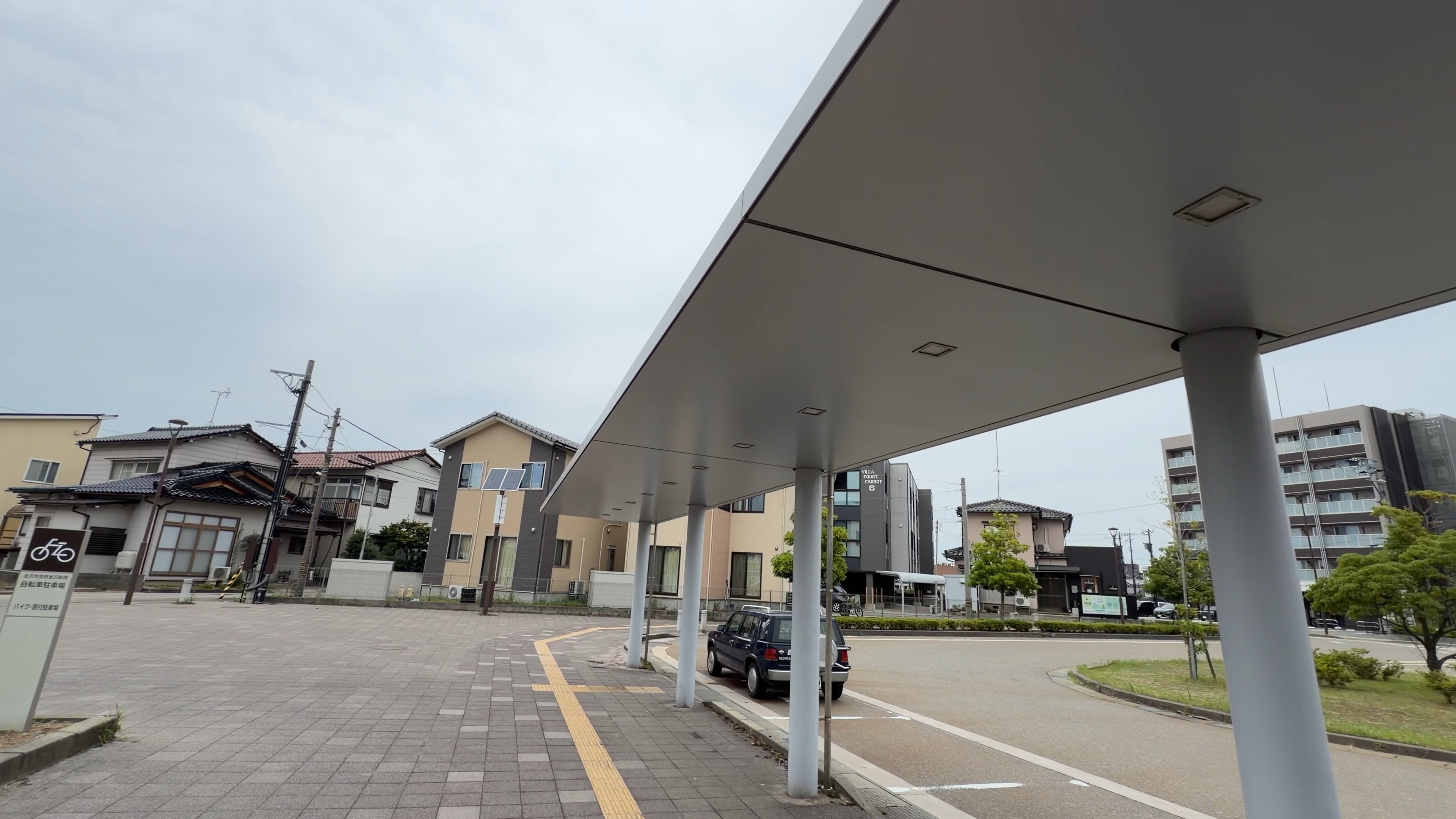 屋根の続く歩道を駅へ戻る道、奥にロータリーと住宅街