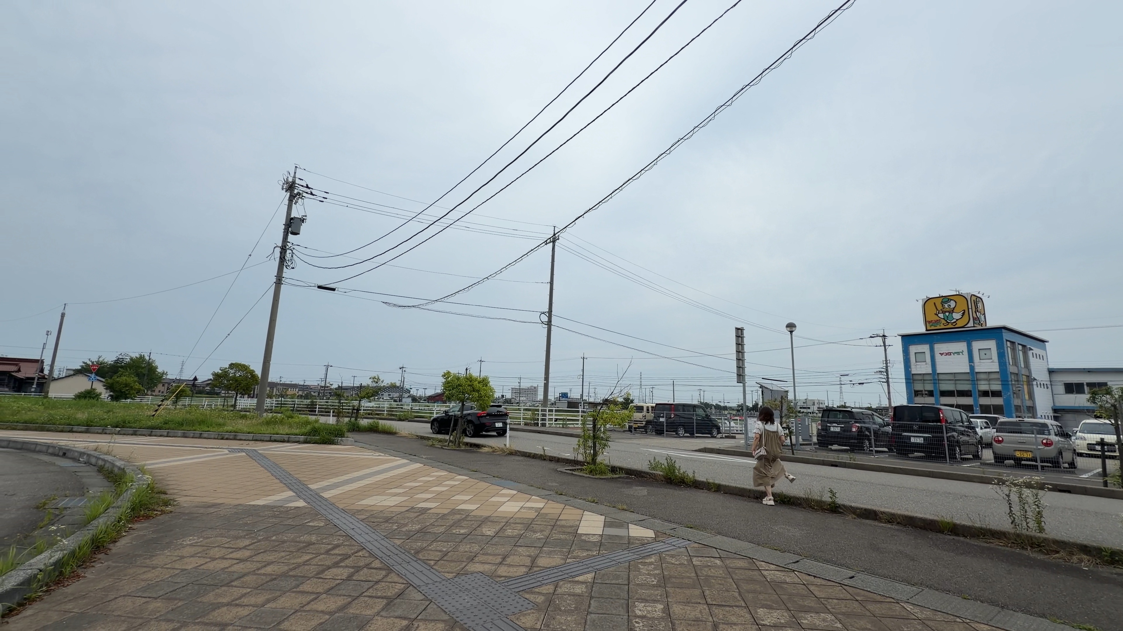 東金沢駅そばの駐車場と青い看板の建物、歩く人の後ろ姿