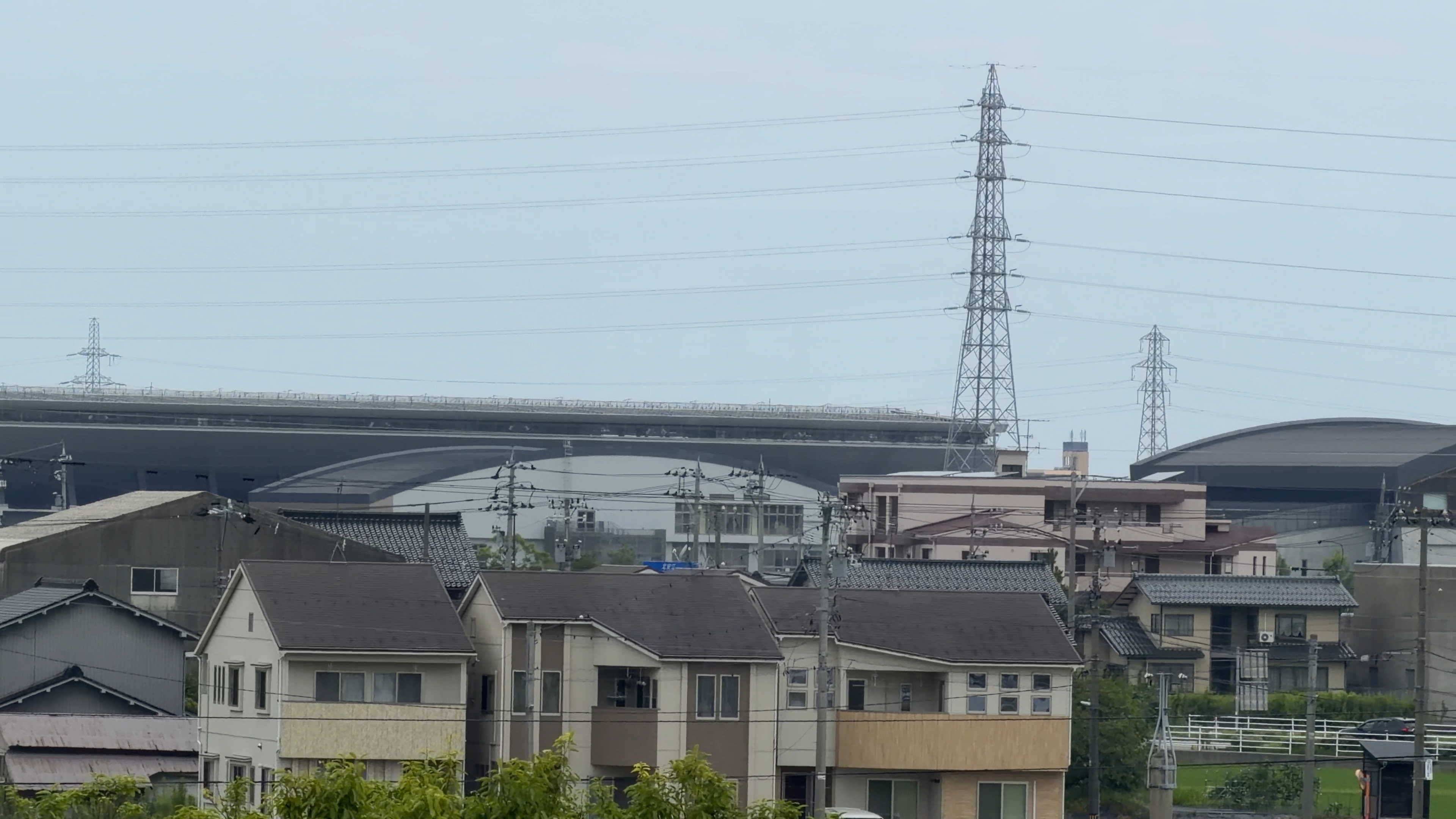 住宅の向こうに見える金沢スタジアムの曲線屋根と送電鉄塔、新幹線高架