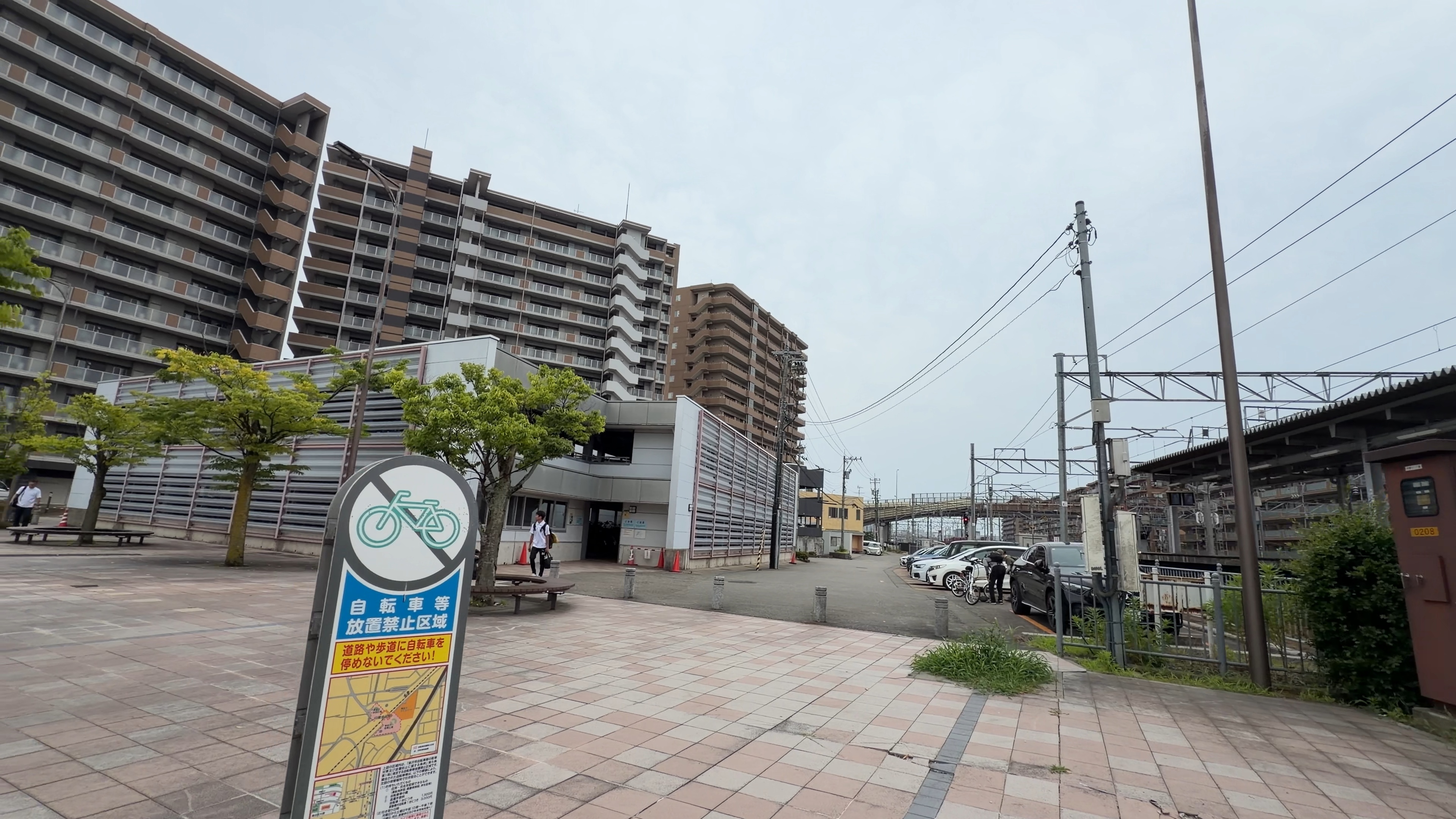 東口の広場全景、高層マンションと駐輪禁止の案内看板、木陰のベンチ
