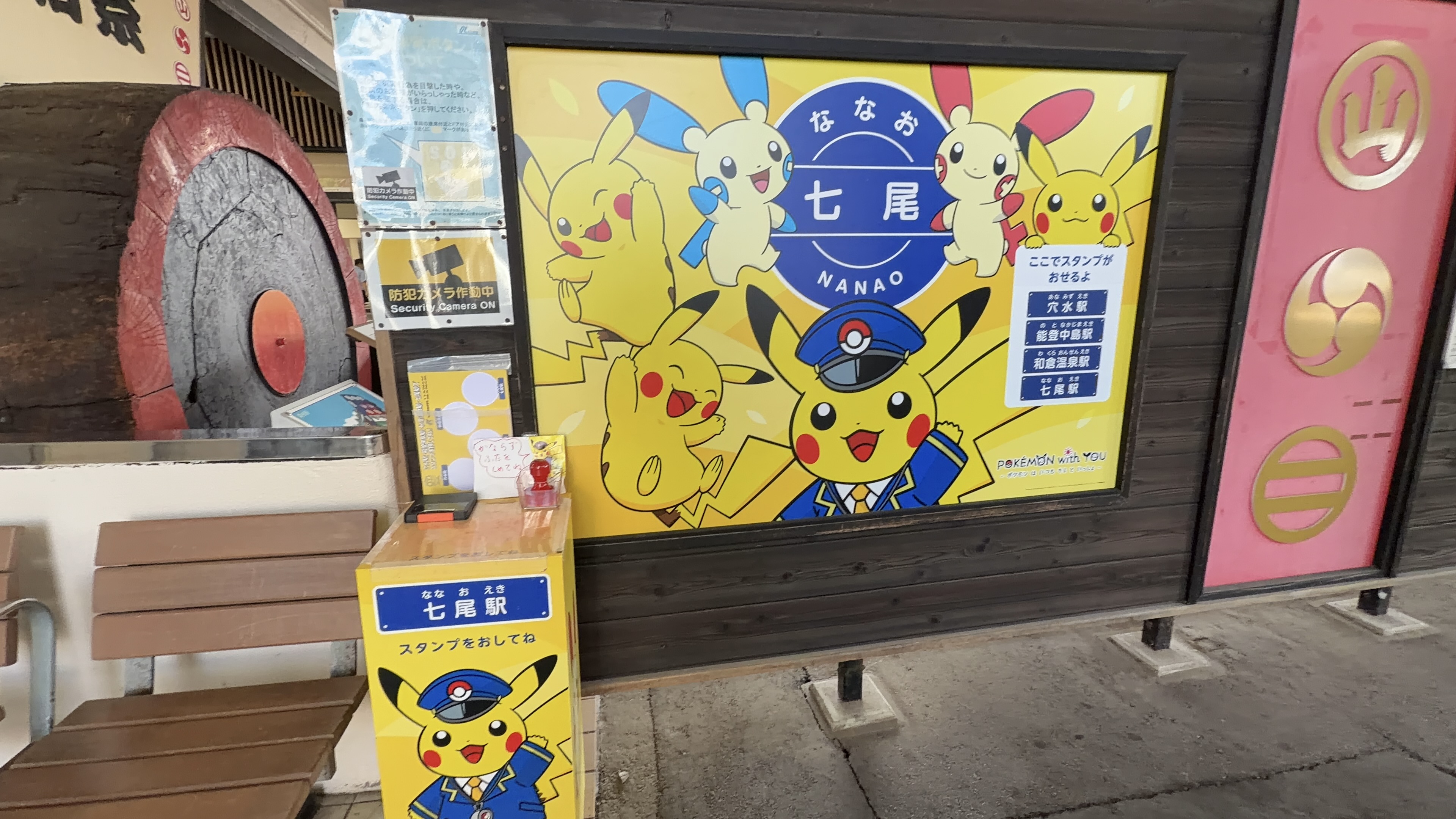 駅舎軒下のポスター、ピカチュウやポケモンたちが描かれた「なな 七尾 NANAO」の看板と、七尾駅のスタンプ台