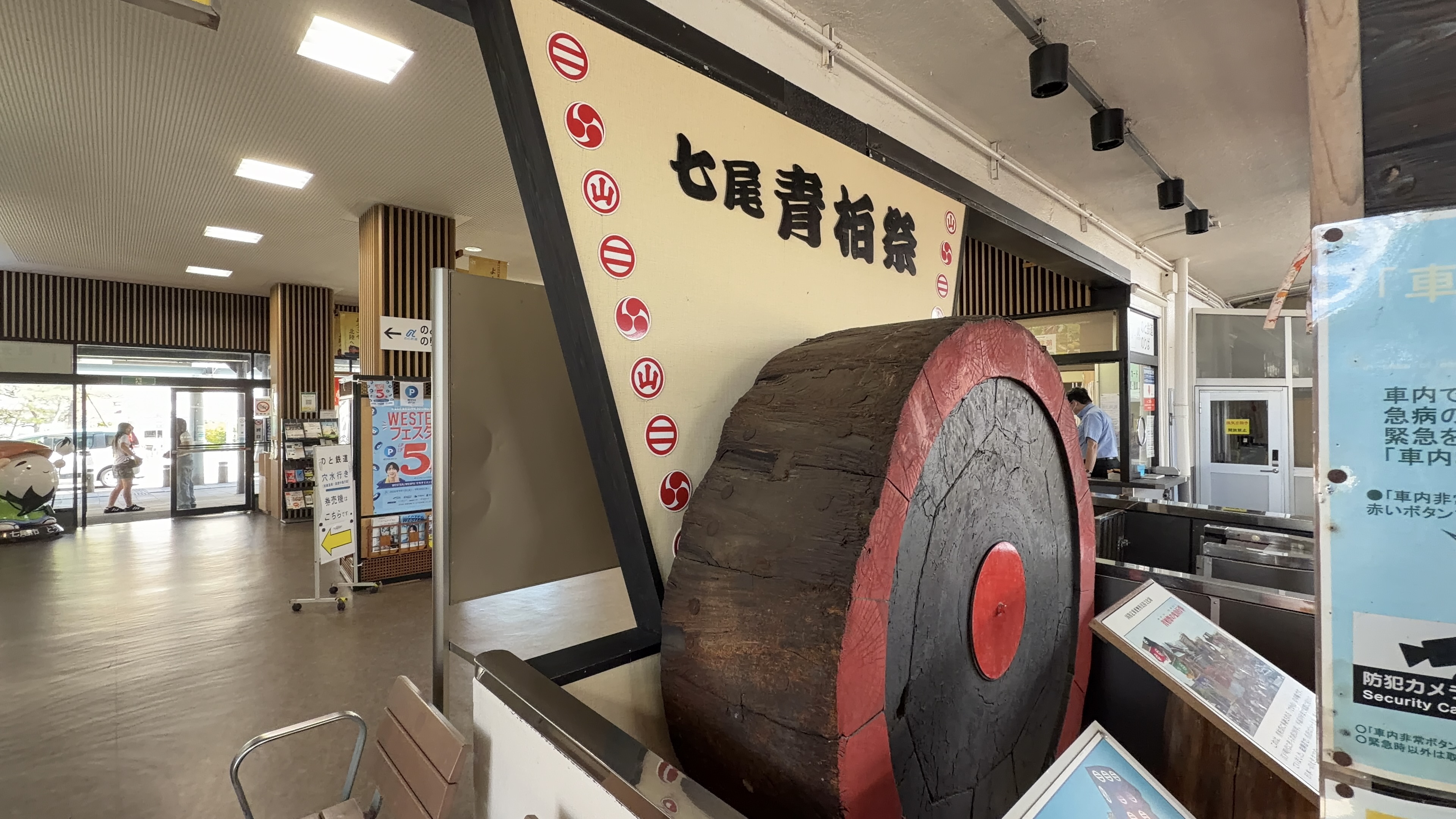「七尾青柏祭」の文字が入った、赤と黒の大きな木の車輪の輪切り、駅舎内の改札そば