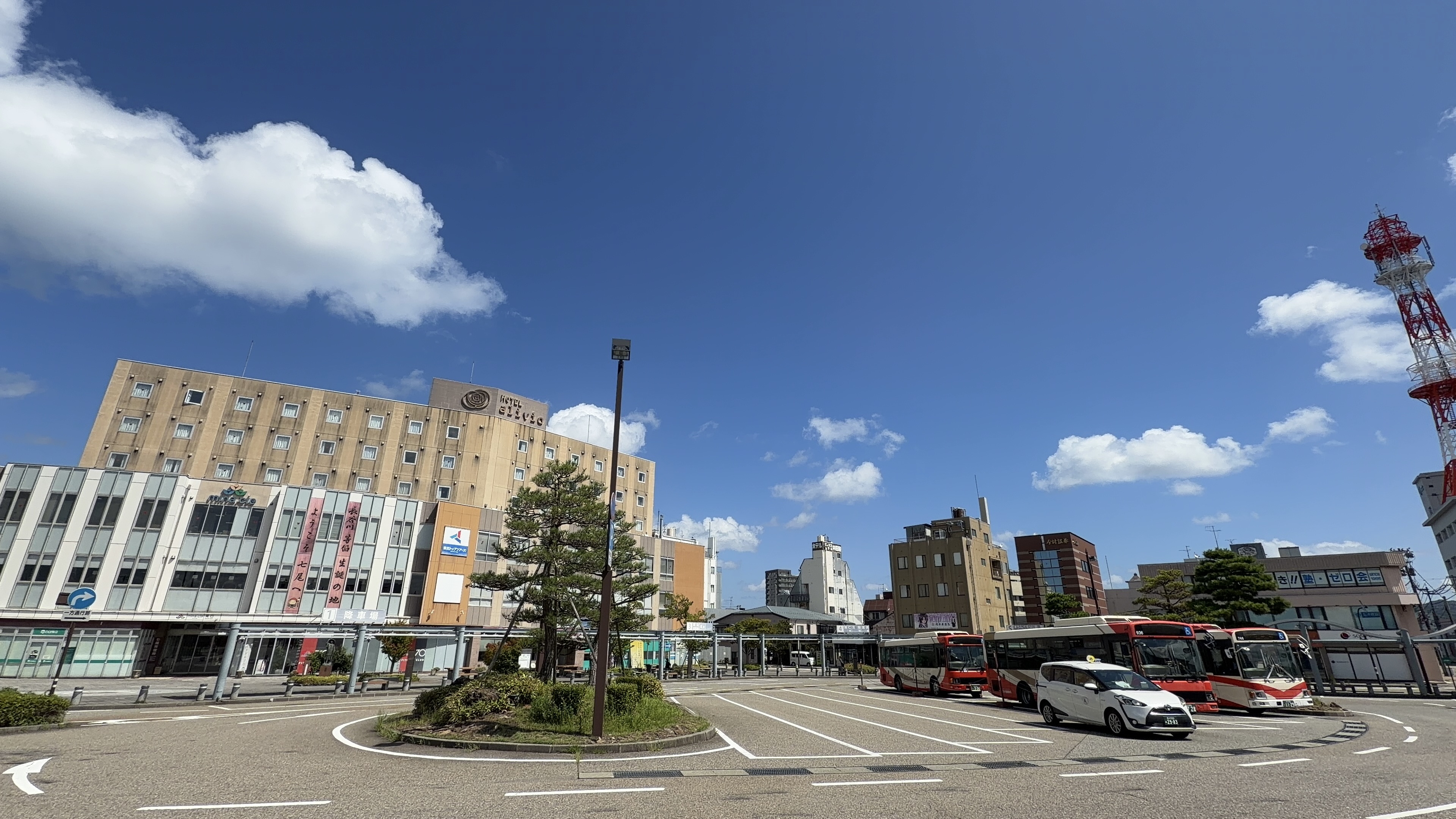 七尾駅前のロータリー、「HOTEL alivio」の建物とバスが並ぶ様子、右手に赤白の電波塔