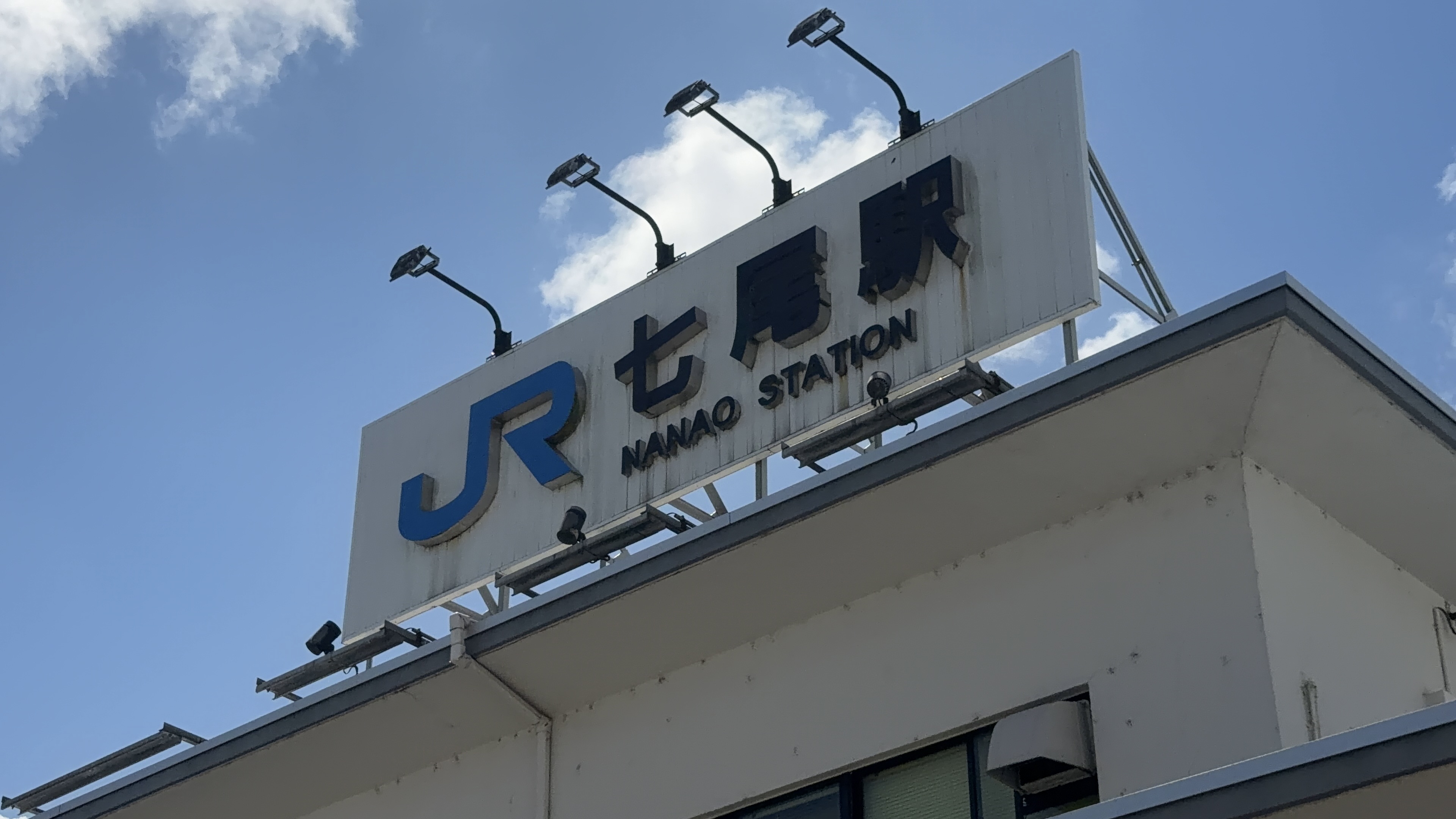 「JR七尾駅 NANAO STATION」の看板のクローズアップ、青空を背景に