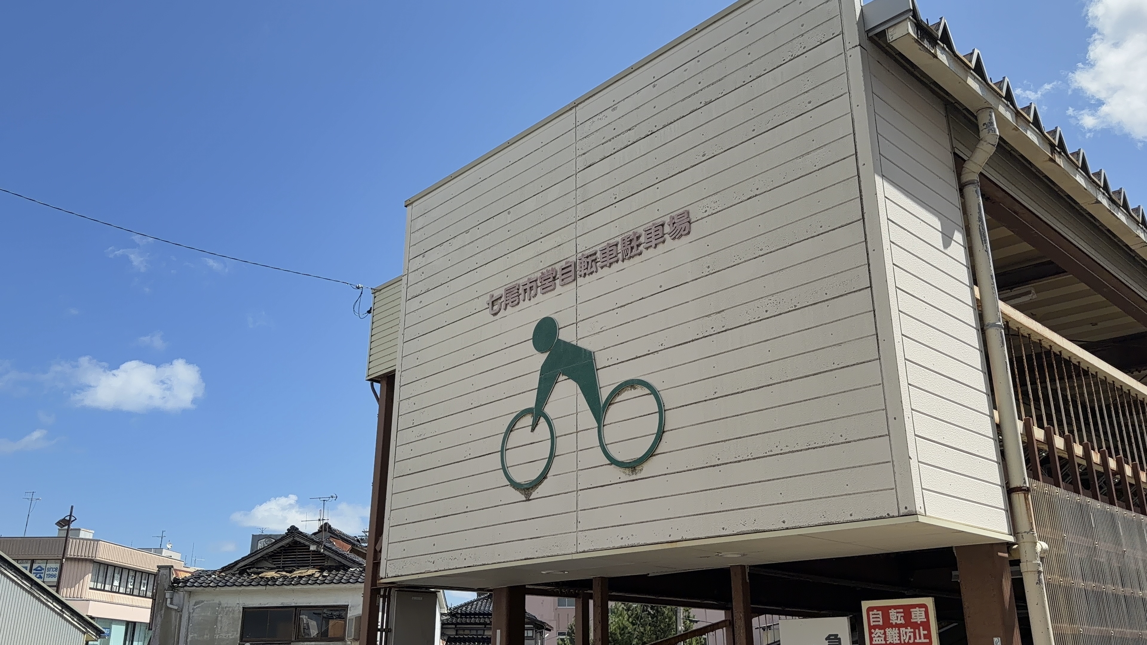 「七尾市営自転車駐車場」の看板、自転車のイラストマーク、高架下の建物