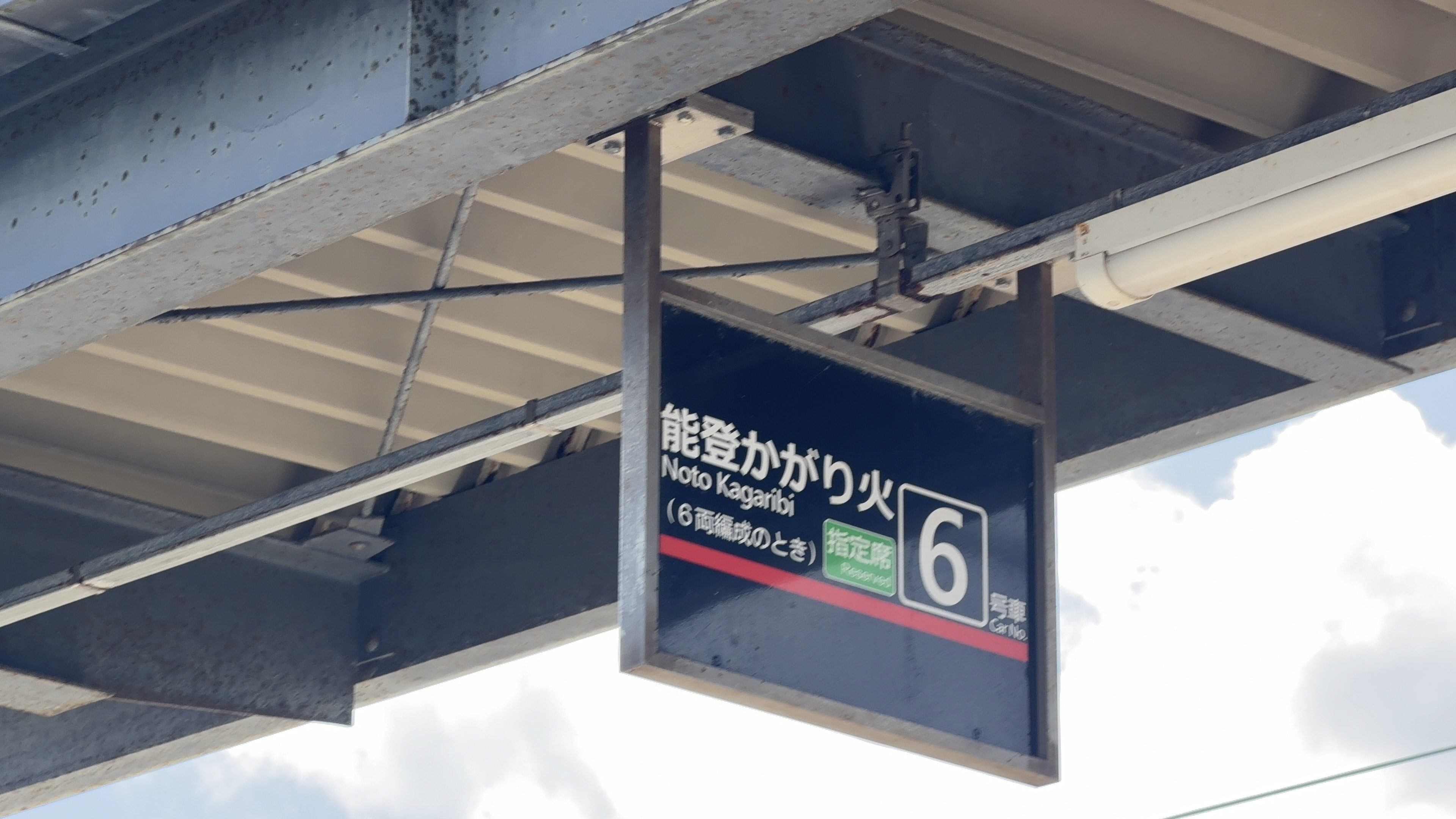 ホーム屋根から吊るされた「能登かがり火 Noto Kagaribi（6両編成のとき）指定席 6号車」の案内板