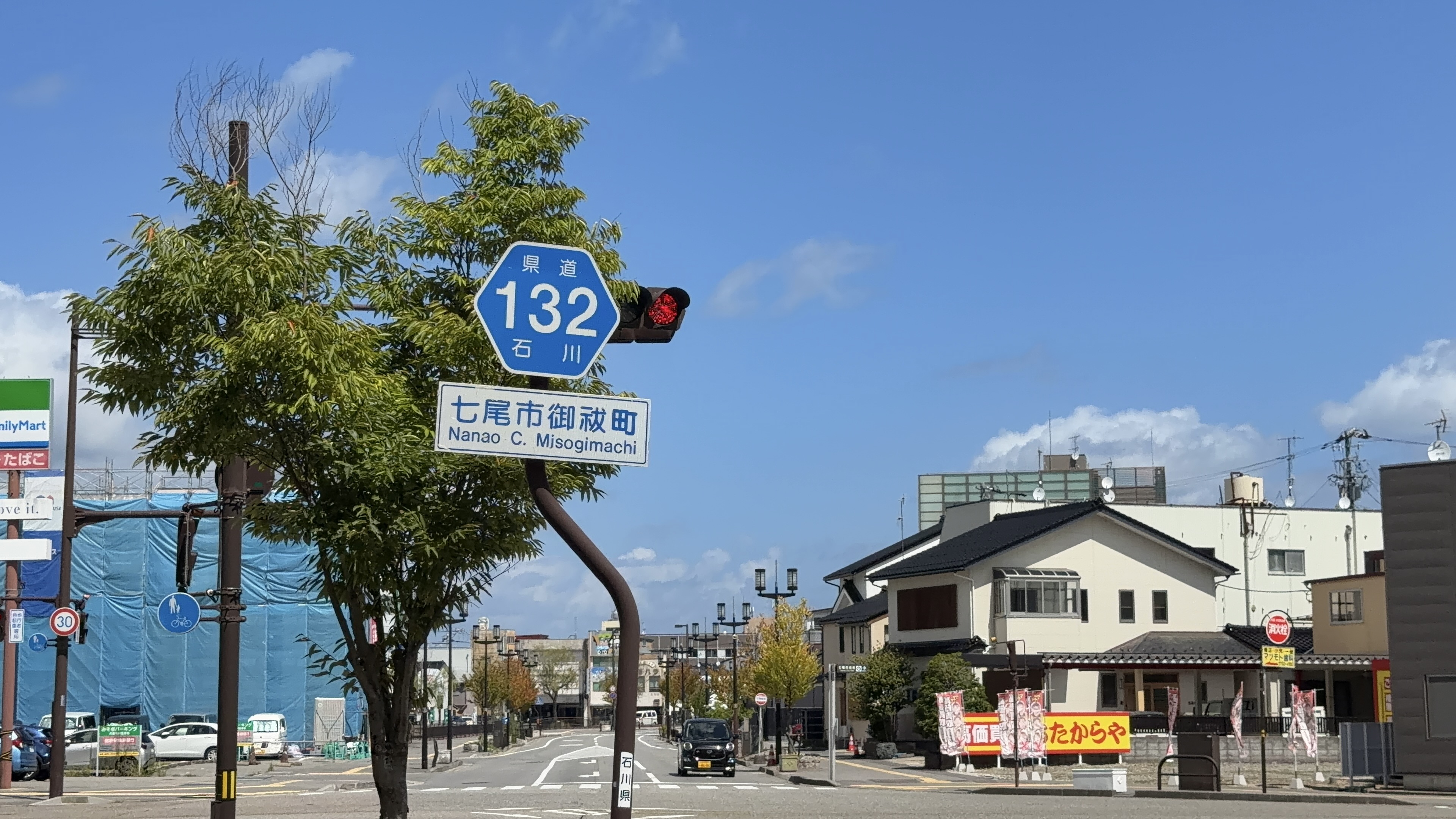青い六角形の「県道132 石川」標識と、「七尾市御祓町 Nanao C. Misogimachi」の地名標識、信号機
