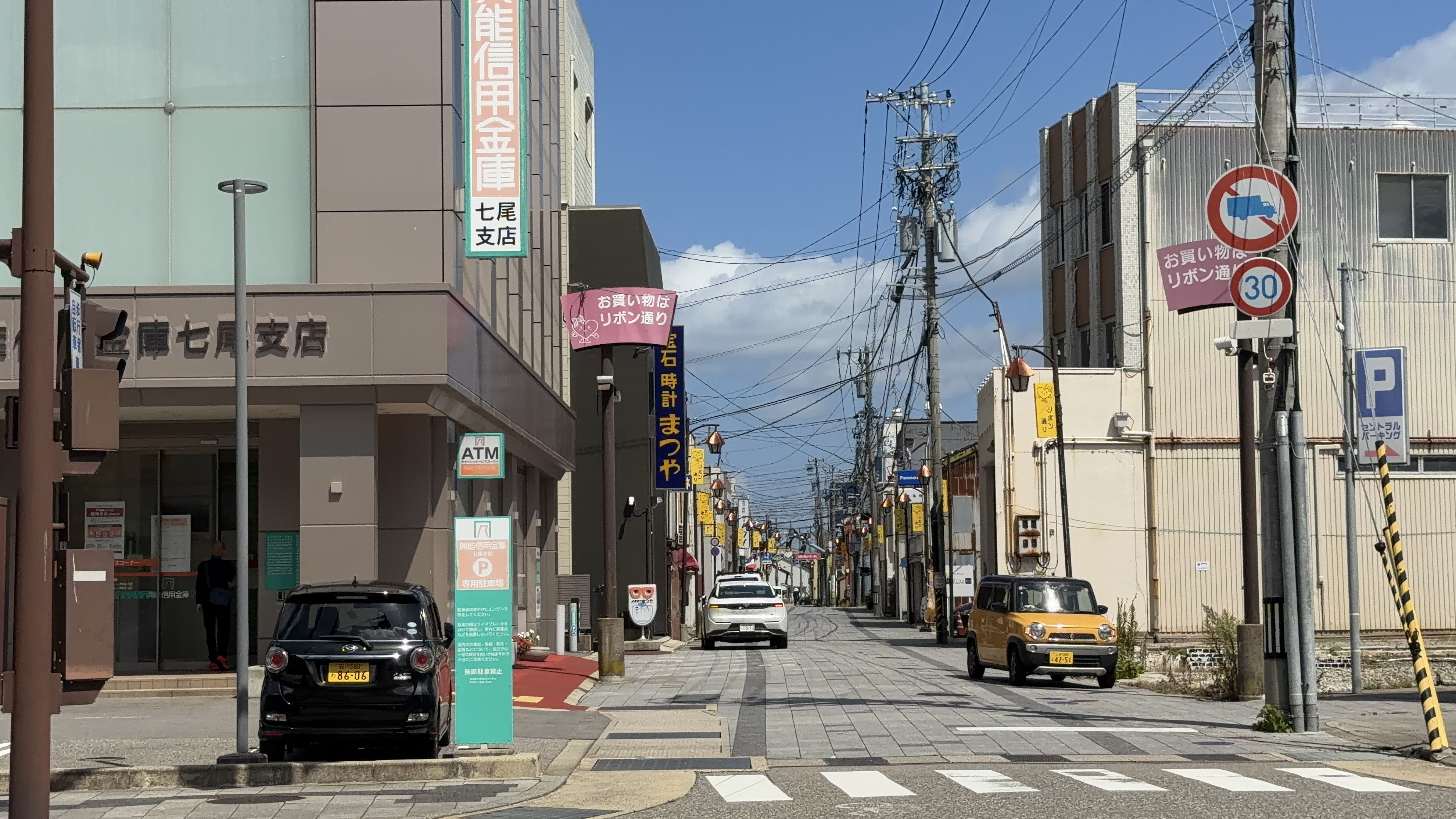 「能登信用金庫 七尾支店」の建物と、「お買い物はリボン通り」のピンクの案内、「宝石時計まつや」の看板