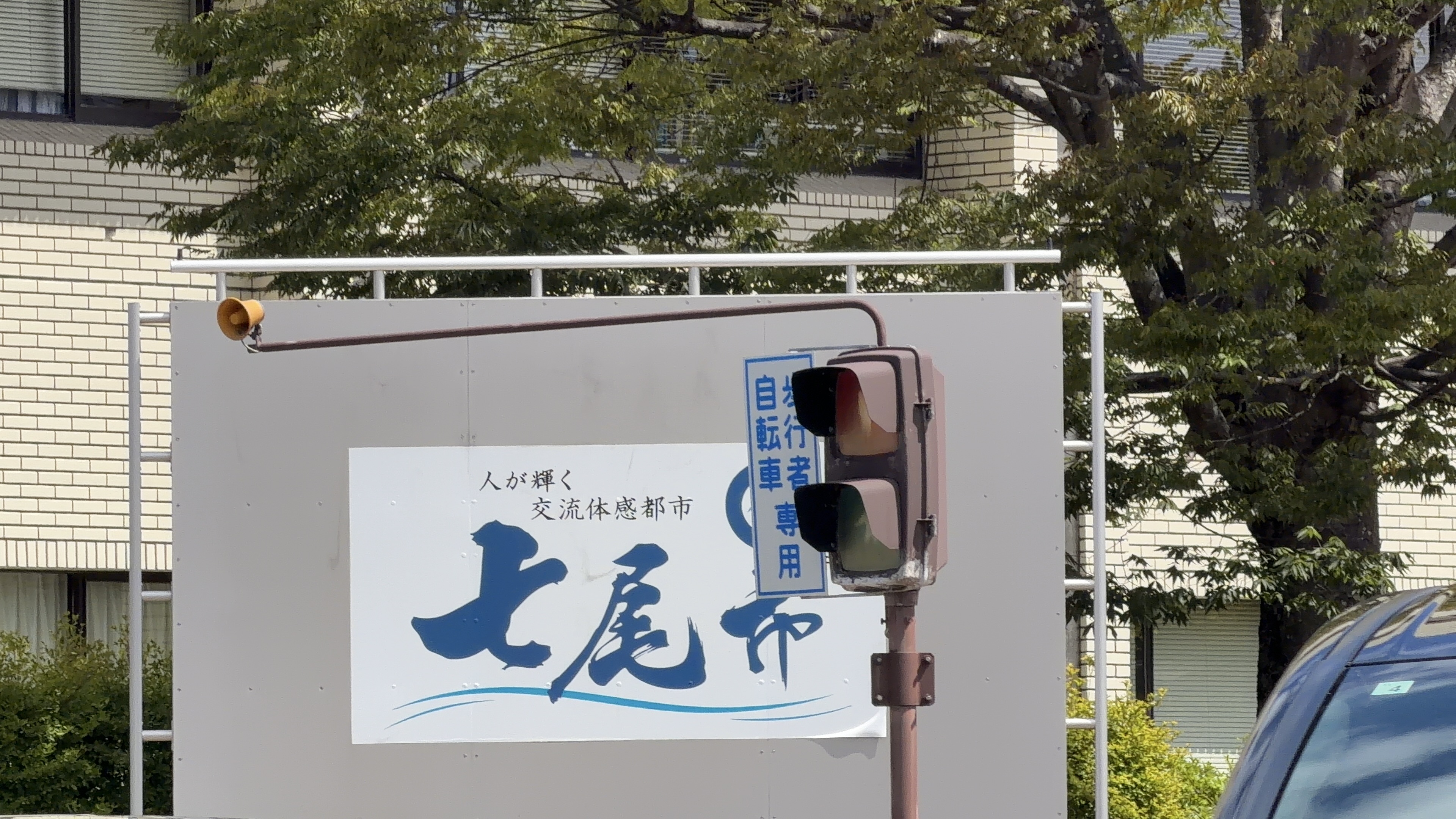 「人が輝く 交流体感都市 七尾市」看板のクローズアップと、歩行者・自転車者専用の信号機