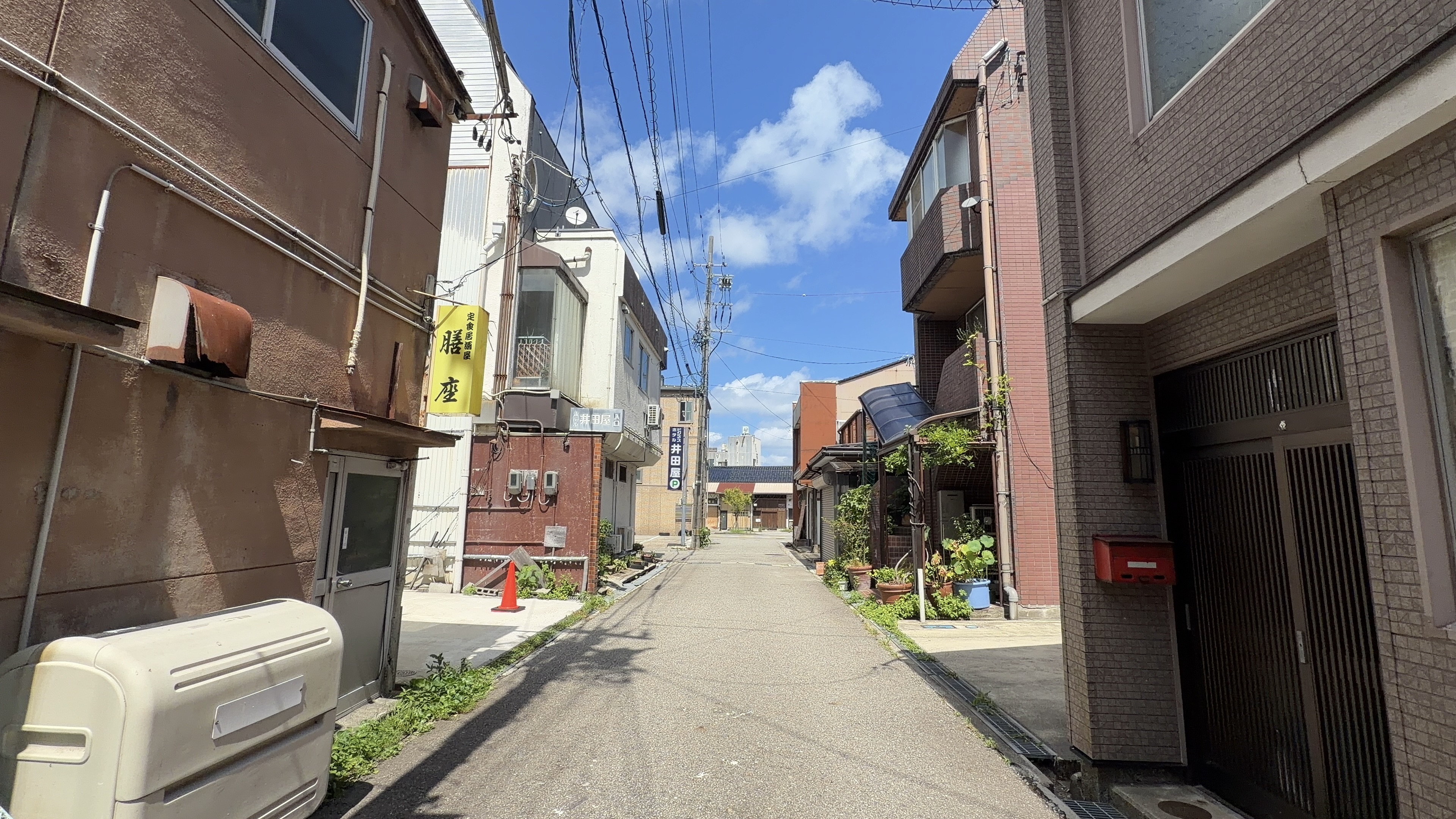 路地の入口、「定食多酒屋 膳座」の黄色い縦看板と、「ホテル井田屋」駐車場入口の案内板