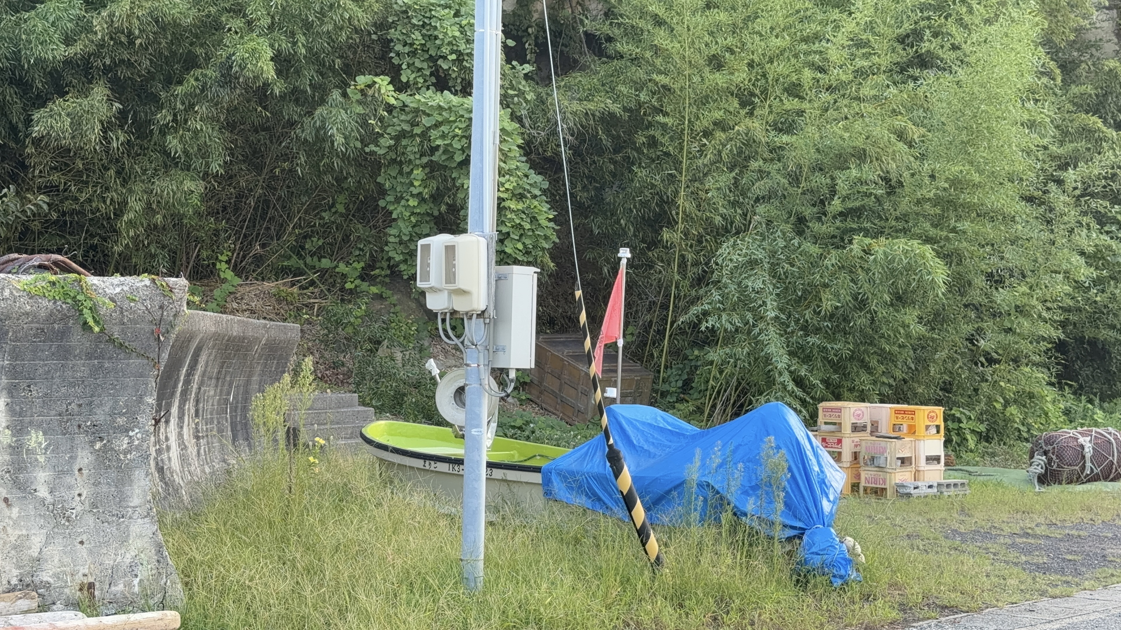 草むらに置かれた小型ボートと、ブルーシートをかぶった荷物