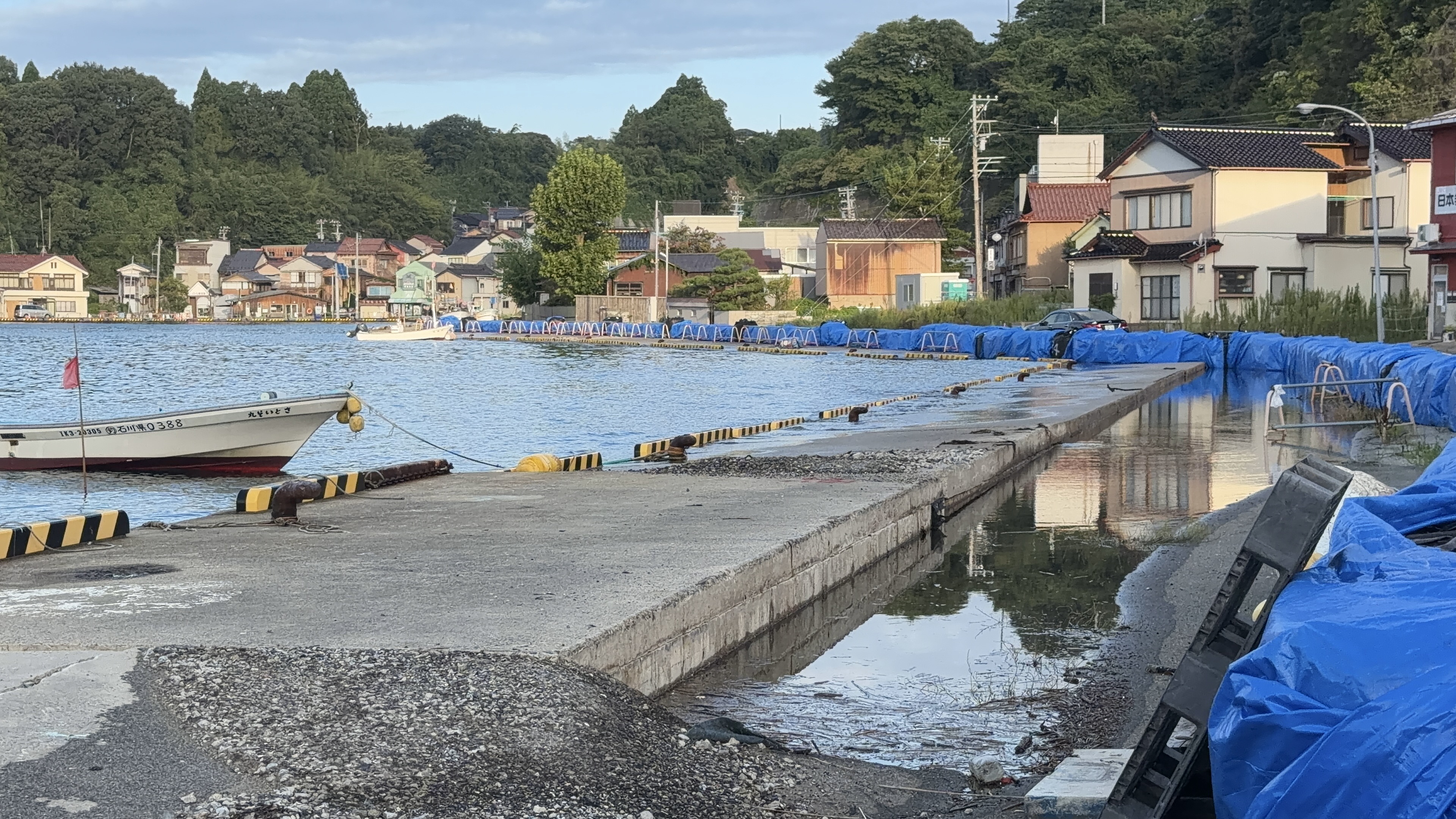 冠水した岸壁と、ブルーシートをかぶった荷物、係留された小舟